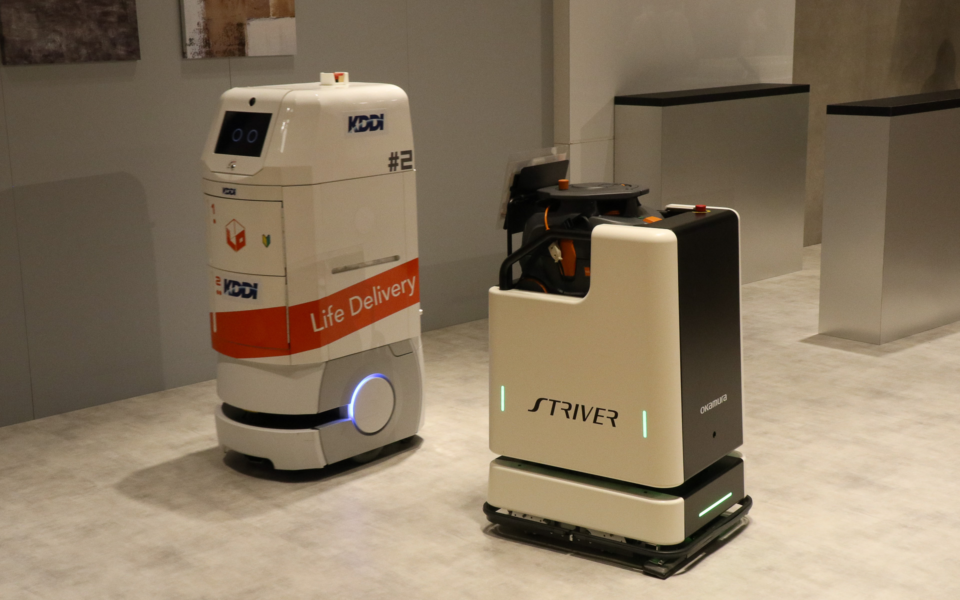 異なるメーカー製のロボットをクラウド管理で協調させるデモ。フロアを掃除する背が低いほうのロボットは常に動き続けているところに、奥で待機している配膳ロボットに飲料水のペットボトルを届けるよう指示を出す。この状況をクラウドに置かれたKDDIの「ロボットプラットフォーム」が管理して、2台のロボットが互いにじゃまをしないようなルートを定めて指示を送り、配膳ロボットはスムーズに手元までペットボトルを届けてくれた