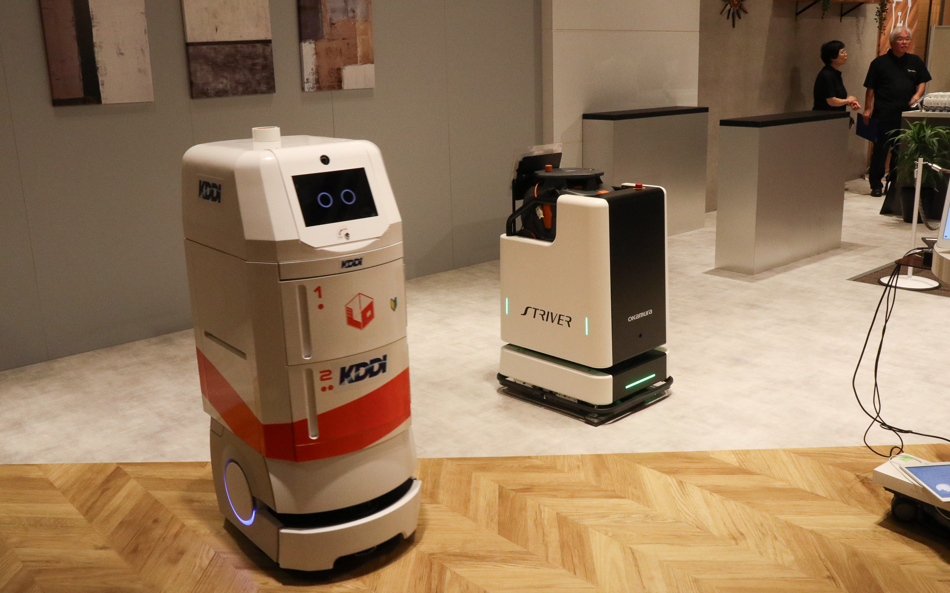 異なるメーカー製のロボットをクラウド管理で協調させるデモ。フロアを掃除する背が低いほうのロボットは常に動き続けているところに、奥で待機している配膳ロボットに飲料水のペットボトルを届けるよう指示を出す。この状況をクラウドに置かれたKDDIの「ロボットプラットフォーム」が管理して、2台のロボットが互いにじゃまをしないようなルートを定めて指示を送り、配膳ロボットはスムーズに手元までペットボトルを届けてくれた