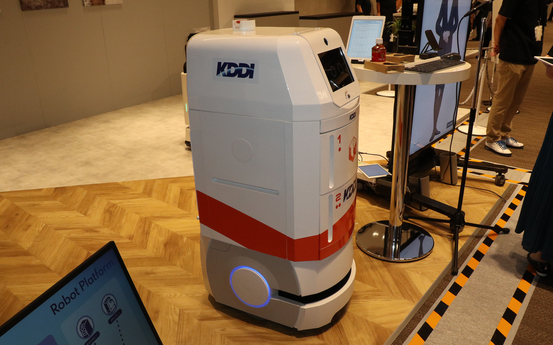 異なるメーカー製のロボットをクラウド管理で協調させるデモ。フロアを掃除する背が低いほうのロボットは常に動き続けているところに、奥で待機している配膳ロボットに飲料水のペットボトルを届けるよう指示を出す。この状況をクラウドに置かれたKDDIの「ロボットプラットフォーム」が管理して、2台のロボットが互いにじゃまをしないようなルートを定めて指示を送り、配膳ロボットはスムーズに手元までペットボトルを届けてくれた