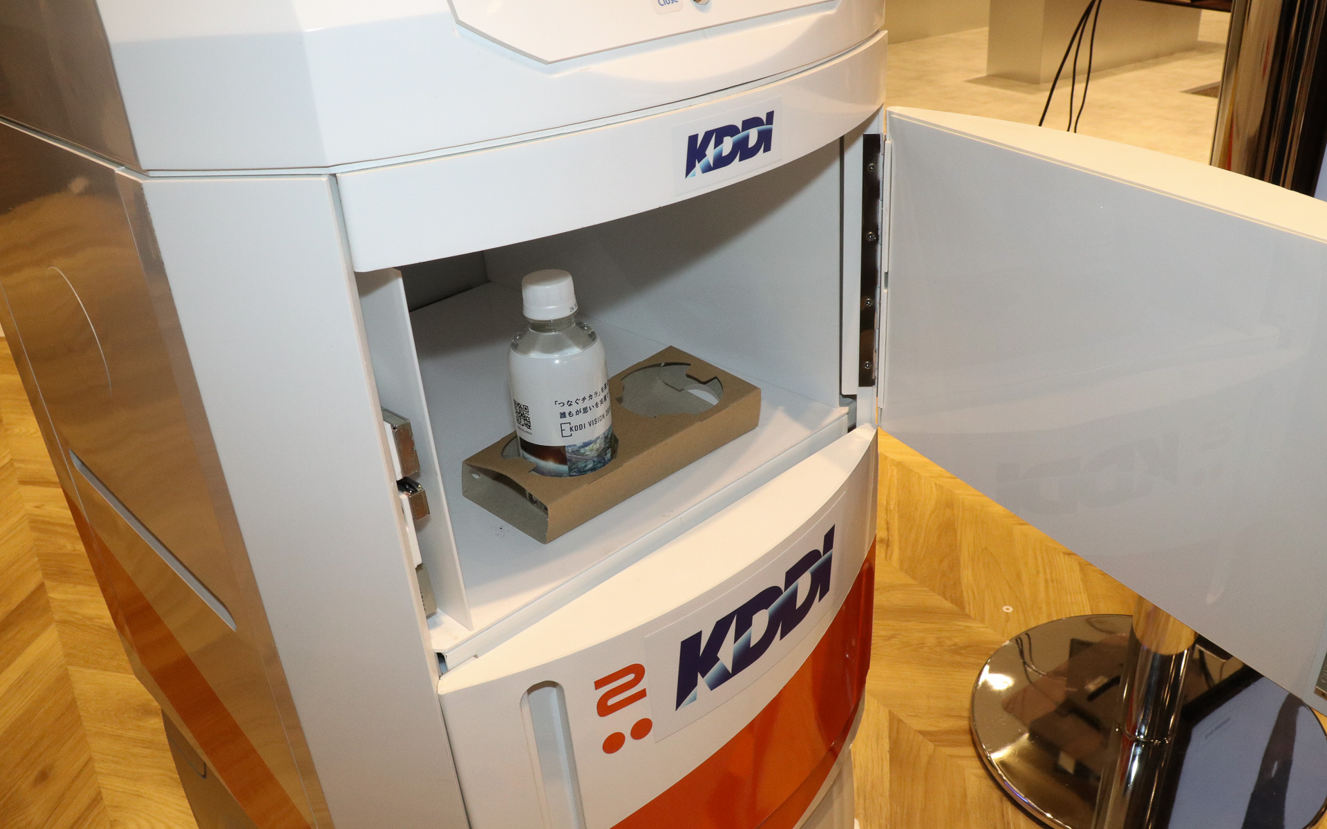 異なるメーカー製のロボットをクラウド管理で協調させるデモ。フロアを掃除する背が低いほうのロボットは常に動き続けているところに、奥で待機している配膳ロボットに飲料水のペットボトルを届けるよう指示を出す。この状況をクラウドに置かれたKDDIの「ロボットプラットフォーム」が管理して、2台のロボットが互いにじゃまをしないようなルートを定めて指示を送り、配膳ロボットはスムーズに手元までペットボトルを届けてくれた