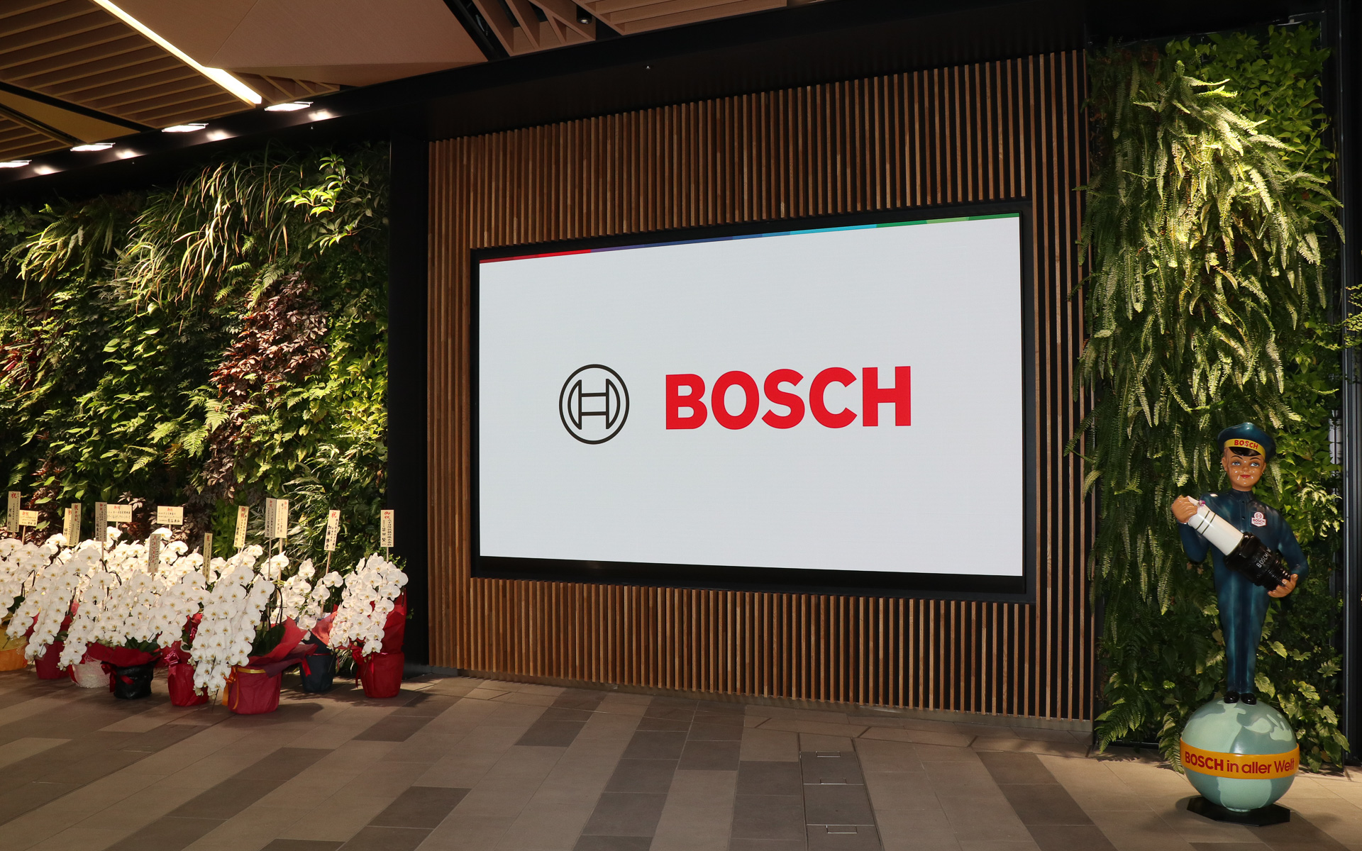 新本社は大地に立つ1本の樹と、その上に広がる空をコンセプトとしており、社屋内に木材を多用し、本物の植物を配したグリーンウォールも各所に設置。スパークプラグを手に持つレトロなデザインの人形も置かれていた