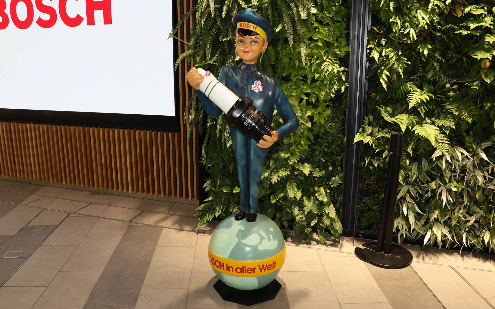 新本社は大地に立つ1本の樹と、その上に広がる空をコンセプトとしており、社屋内に木材を多用し、本物の植物を配したグリーンウォールも各所に設置。スパークプラグを手に持つレトロなデザインの人形も置かれていた