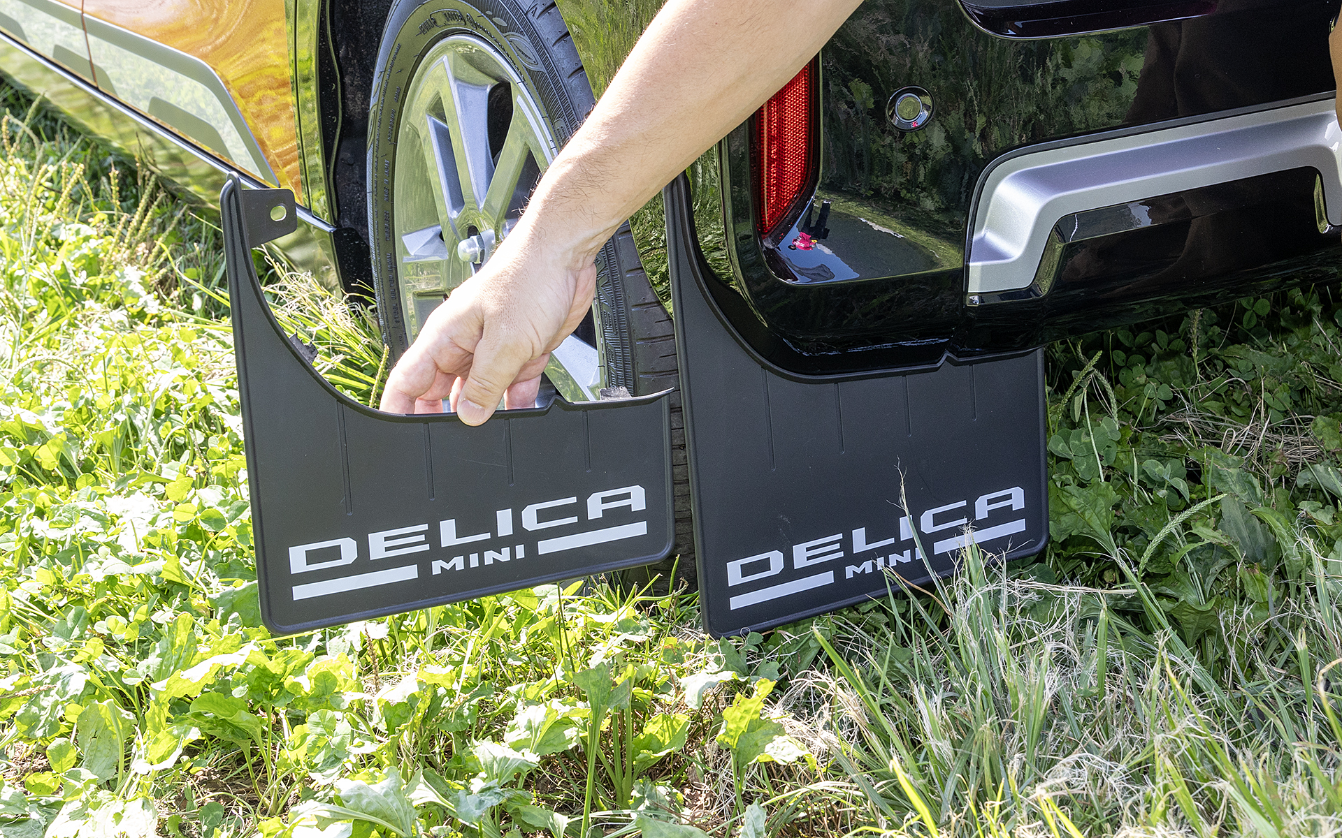 デリカミニには試作のマッドガードが付けられていた。手で持っているのが現在発売中のもの。試作品は全長が長くなっている