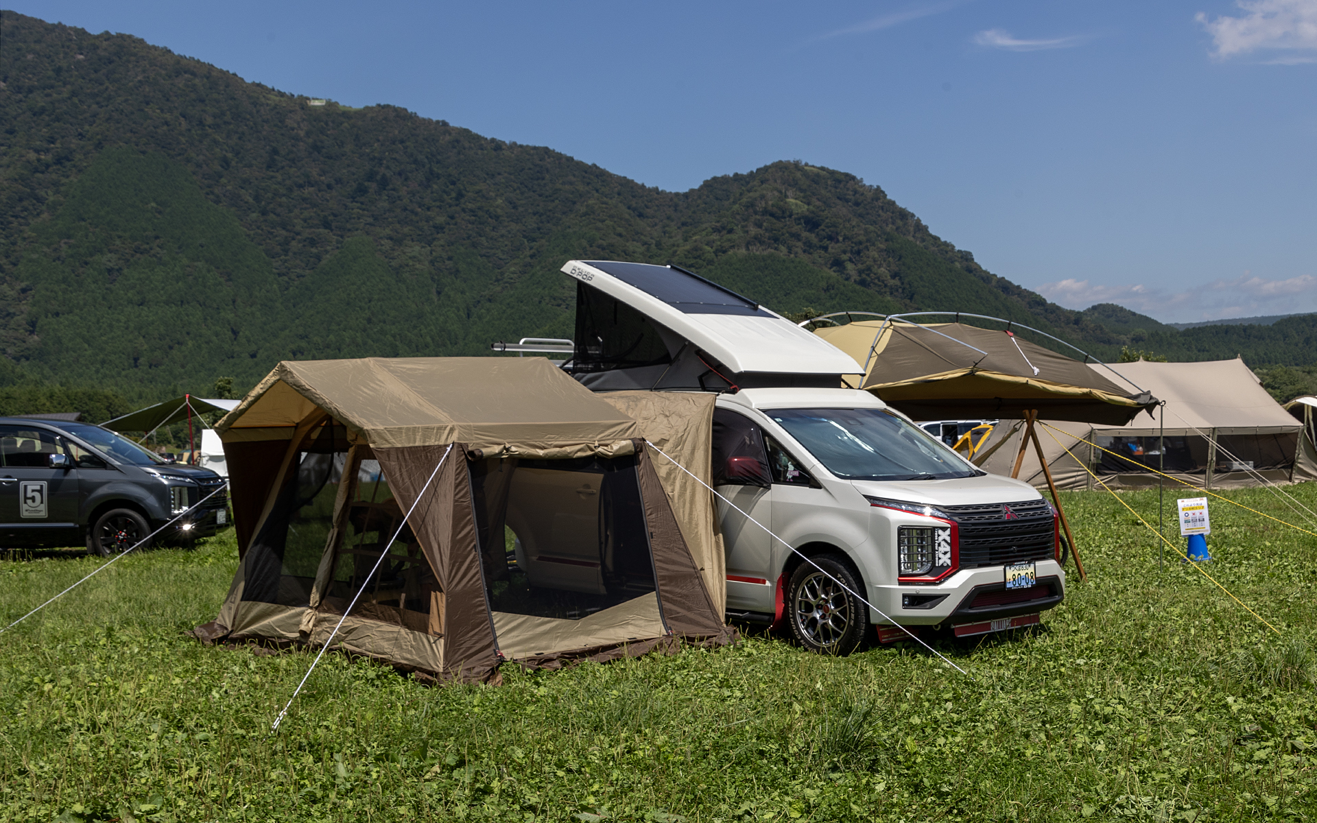 オートキャンプの場合、テントとは別にくつろげるスペースをタープなどで作ることが多い。会場で見かけたスタイルを紹介。こちらはポップアップルーフ付きのデリカD:5にカーサイドタープ＆リビングテントのフル装備