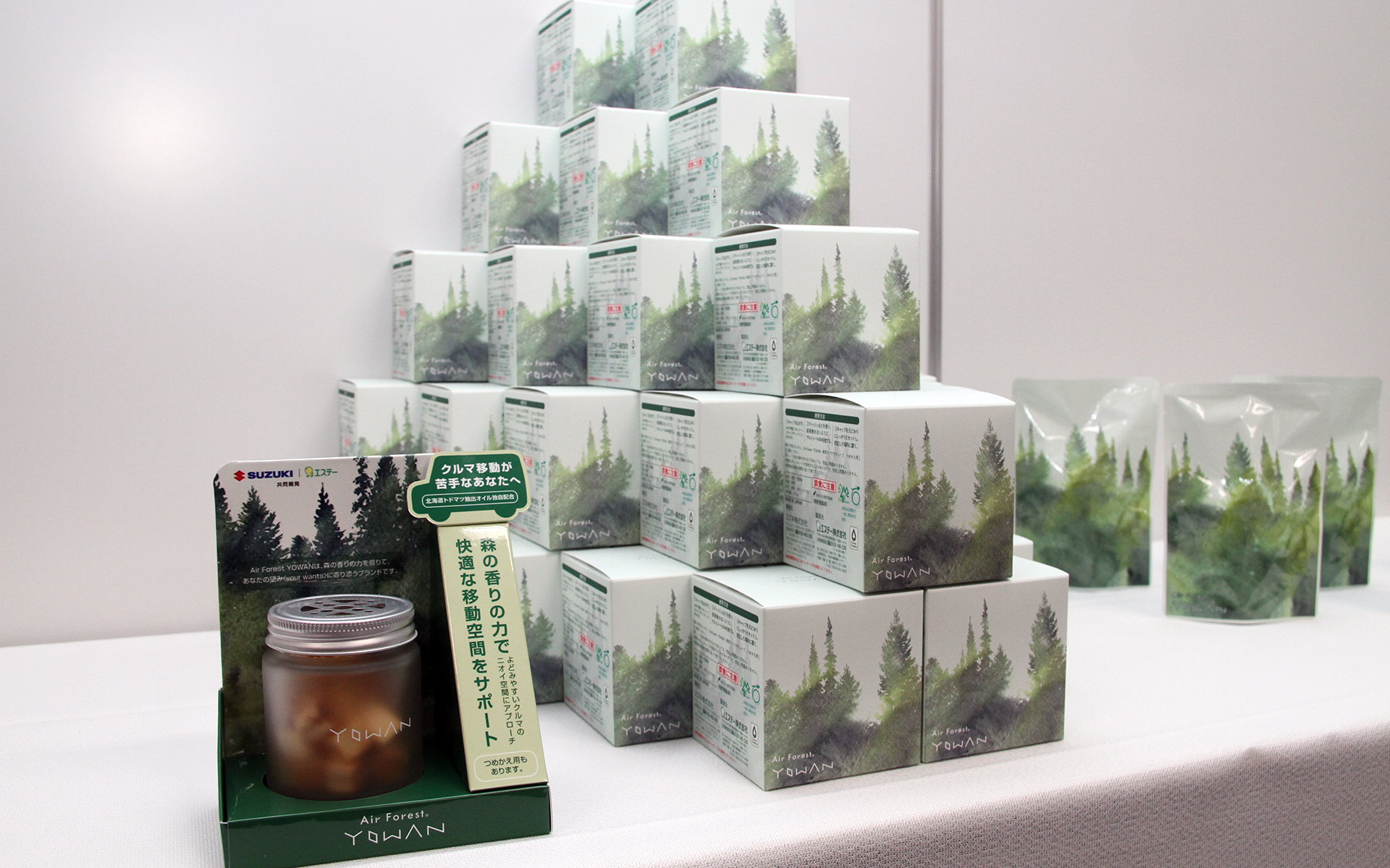 「Air Forest YOWAN車用エアケアキューブ」のパッケージには水彩画タッチのイラストでトドマツの森林が描かれ、森の静けさとすがすがしい空気を表現。一番右にあるのが別売りの詰め替え用パッケージ