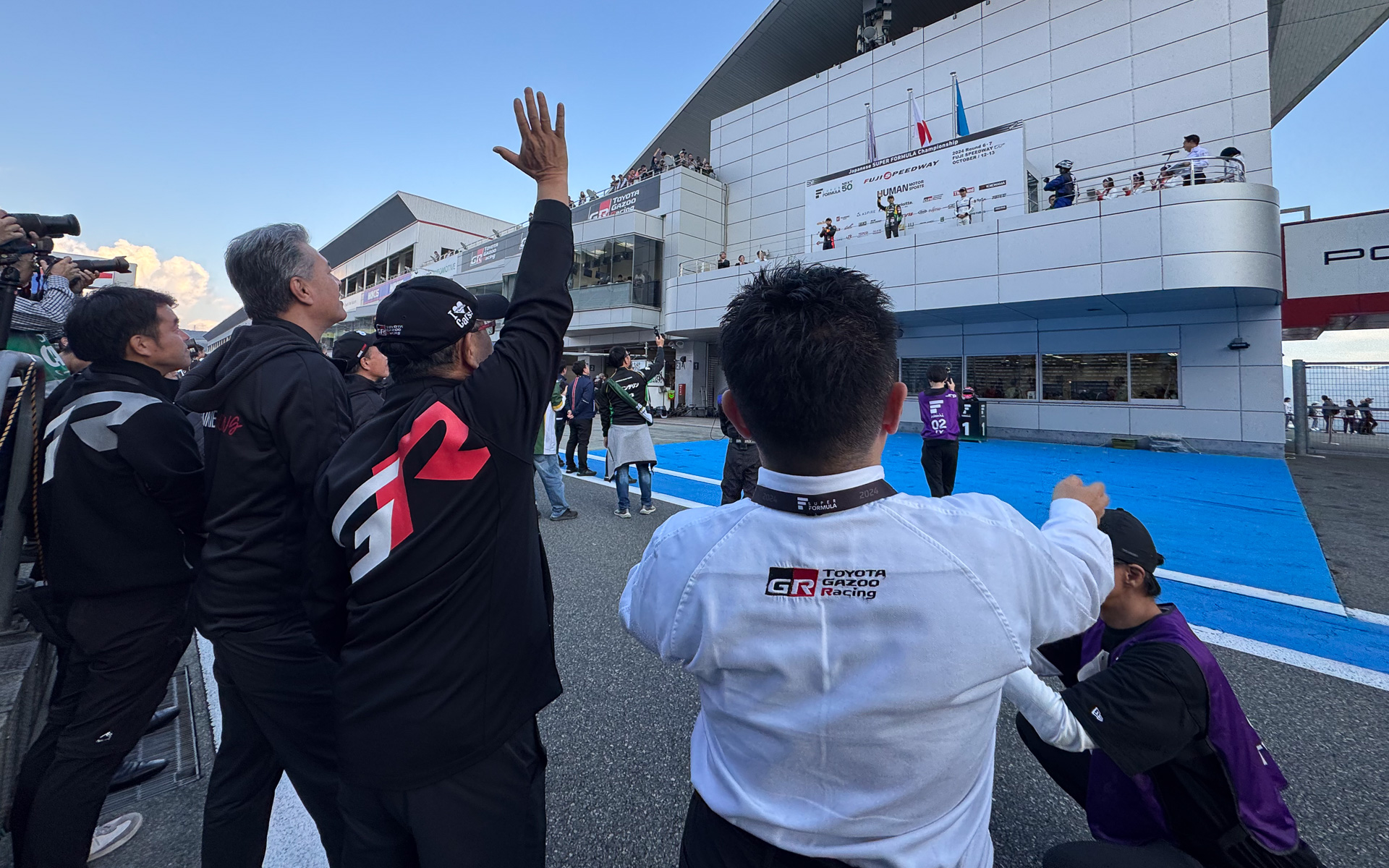 表彰台を獲得した坪井選手、小林可夢偉選手に手を上げてたたえる豊田章男会長。左は中島裕樹副社長、右は高橋智也GRカンパニープレジデント