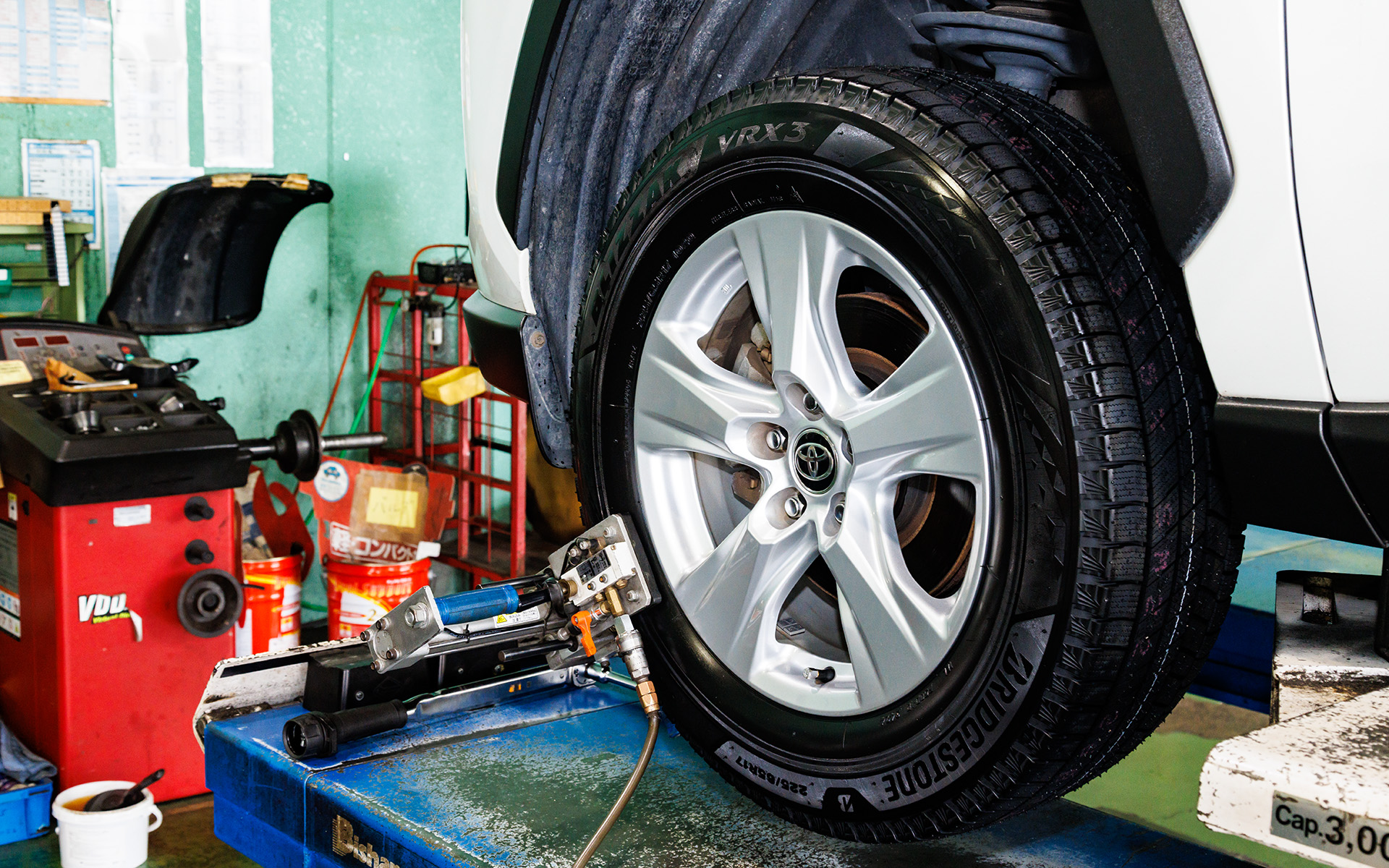 今回ブリザック VRX3の装着をお願いしたのは愛知県春日井市にある「タイヤ館 春日井」。サマー/スタッドレスタイヤの用意はもちろん、3Dアライメントテスタ－を完備するなど足まわり全般の相談に快くのってくれる。また、ブリヂストンが特許技術を持つ「B-SYSTEMセンタリングマシン」も用意。この機器を取り付けることでタイヤに振動を与え、ホイールがしっかりとセンターに合わさった状態でナットを締め込むことができる