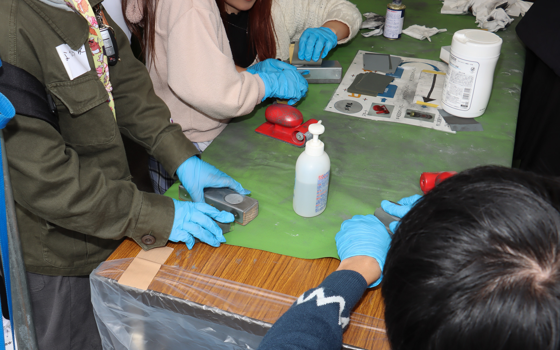 モノづくり体験ブースではイベント参加の記念品にもなるメダル作成を実施。事前に打ち抜かれて片面に刻印したメダルの無地面に油圧プレスでロゴを刻印したあと、紙やすりと研磨剤を使ってピカピカに磨き上げていく