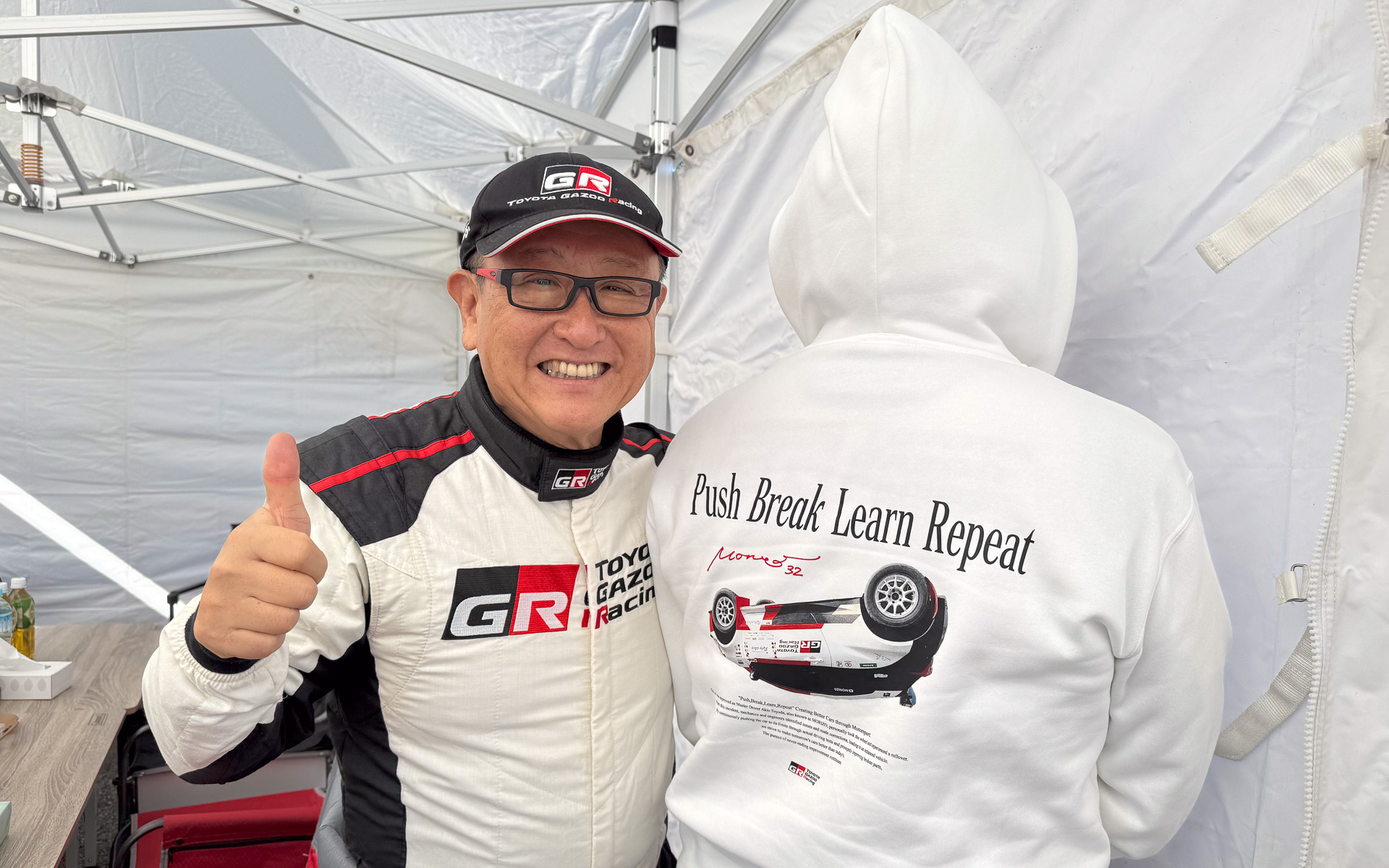 トヨタ自動車 代表取締役会長 豊田章男氏。ラリージャパンで発売した「走る、壊す、直す」の逆さGRヤリスウェア（モデル、山本シンヤ氏）とともに