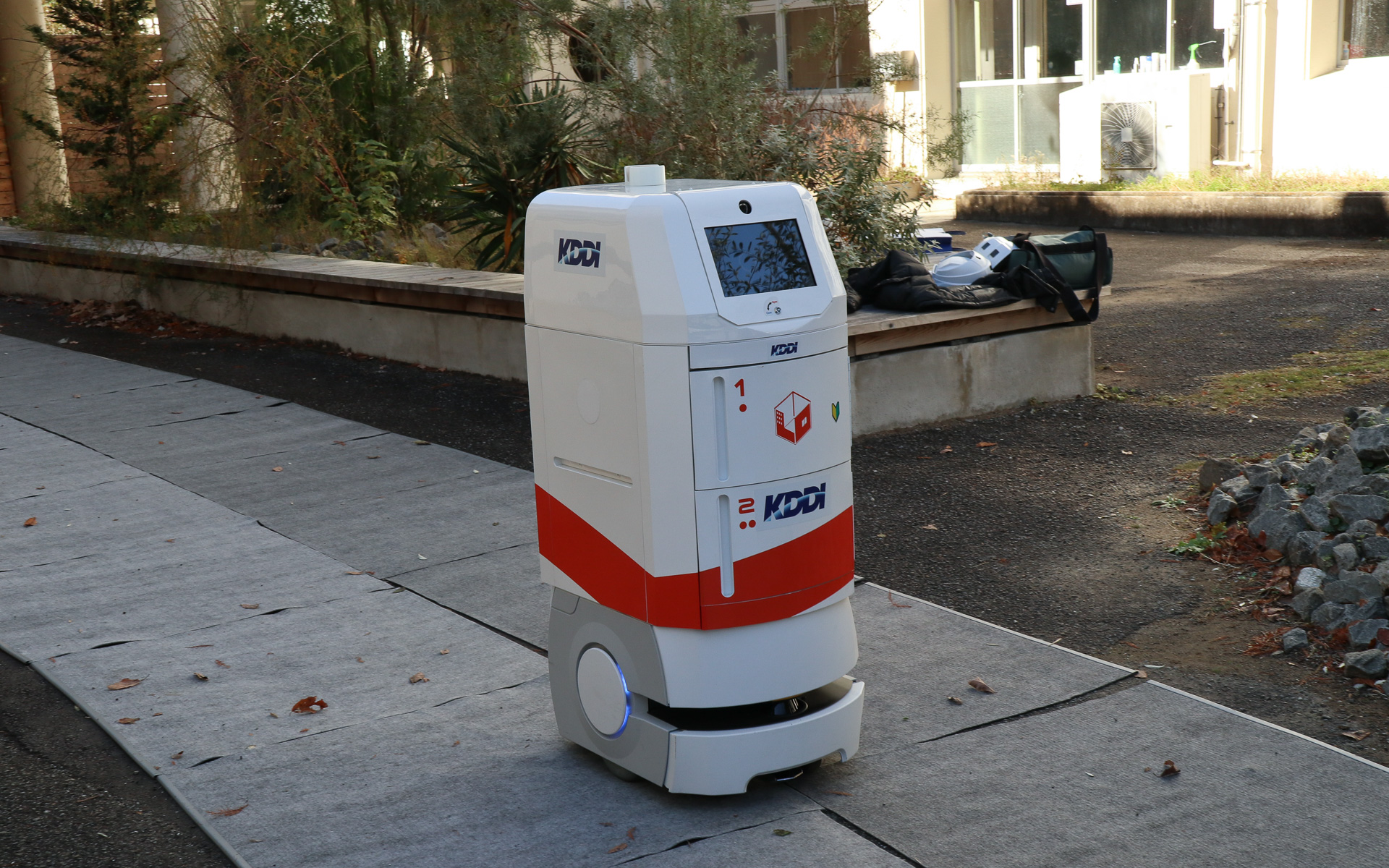 配送ロボットのスタートと連動して自動運転車が校門前のロータリーに走ってきて、どちらかが待つことなく同タイミングで合流