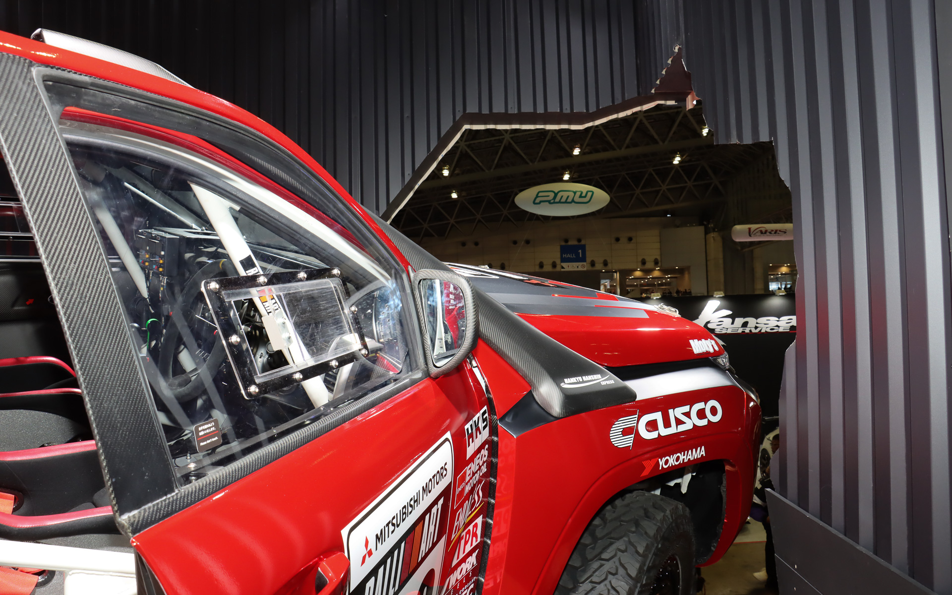 まるでトライトン AXCR 2024 ラリーカーが壁を突き破って飛び出そうとしているような斬新なスタイルで車両展示