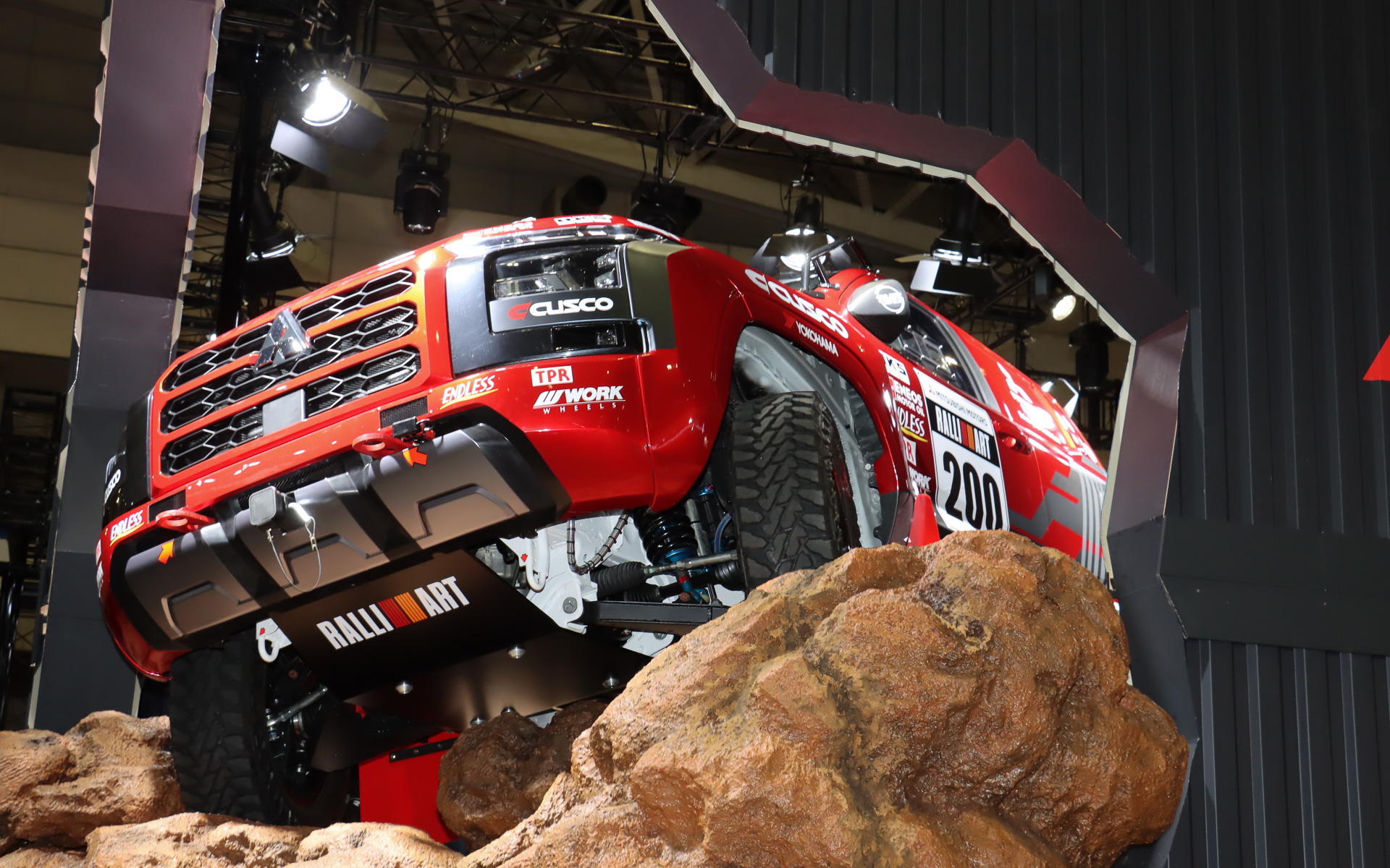 まるでトライトン AXCR 2024 ラリーカーが壁を突き破って飛び出そうとしているような斬新なスタイルで車両展示