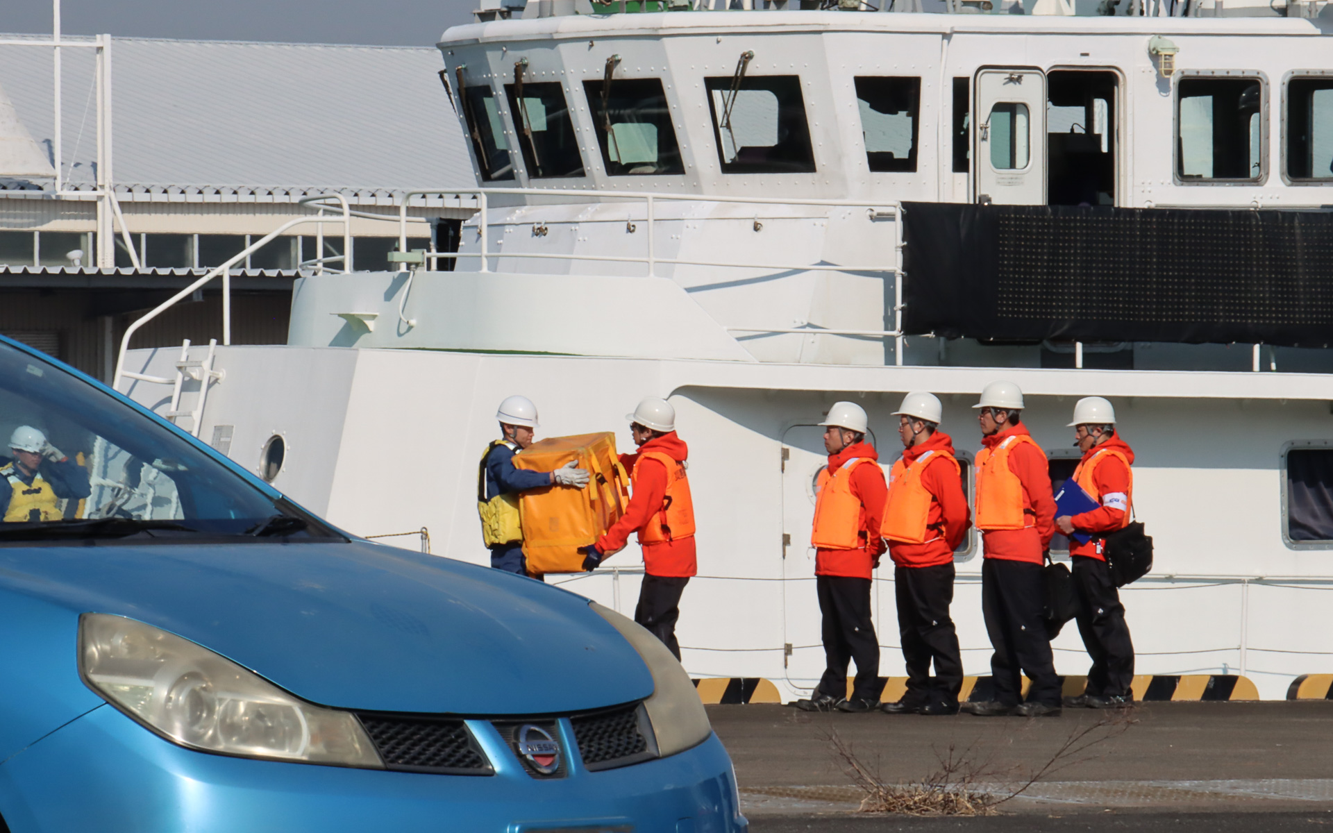 海上保安庁の巡視艇「はまなみ」からKDDI 現地復旧班が下船し、海上保安庁の職員からStarlink復旧機材を受領。雨や海水の影響で浸水被害が出ないよう、各機材は防水カバーで覆われている