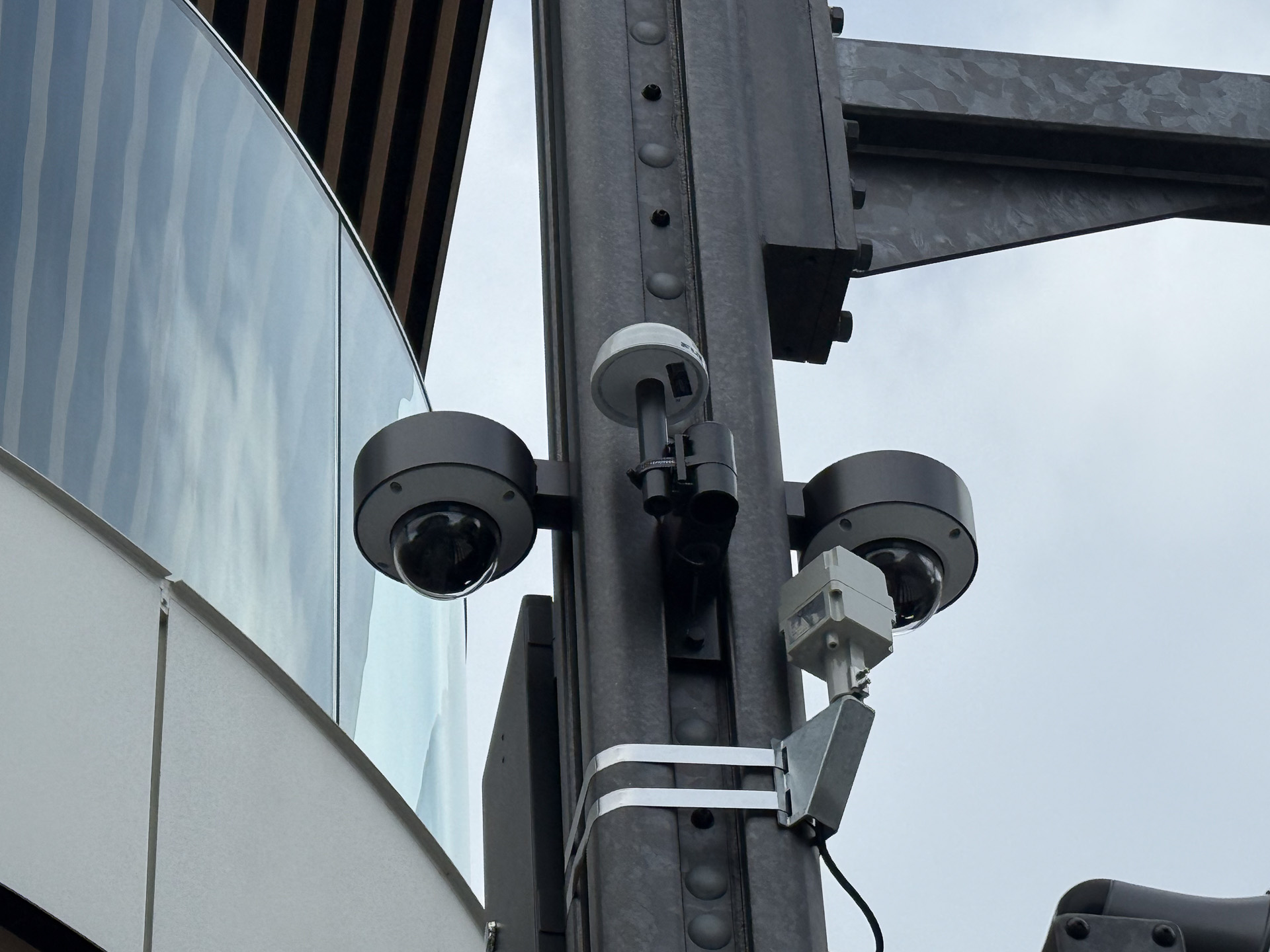 スマートポールに取り付けられたカメラ（下向きの全周レンズを持つデバイス）。2個が組み合わされているように見える。手前のきのこの山のようなものがGNSSアンテナ。右下の四角い白い箱がGPSSアンテナ