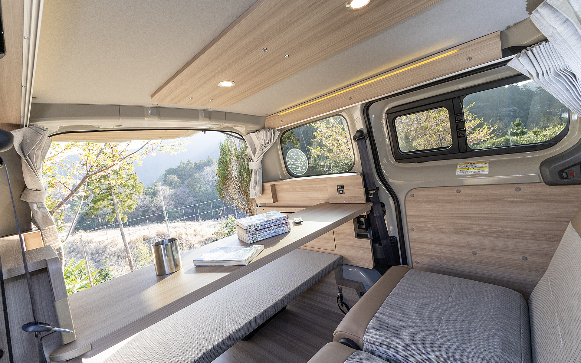 リビングモードにしてスライドテーブルを引き寄せた状態。バックドアを開けておくと景色を眺めながらくつろげる。足下はフロアに降ろしても楽な姿勢を取れるし、平置きベッド部に載せると真っ直ぐ伸ばせる