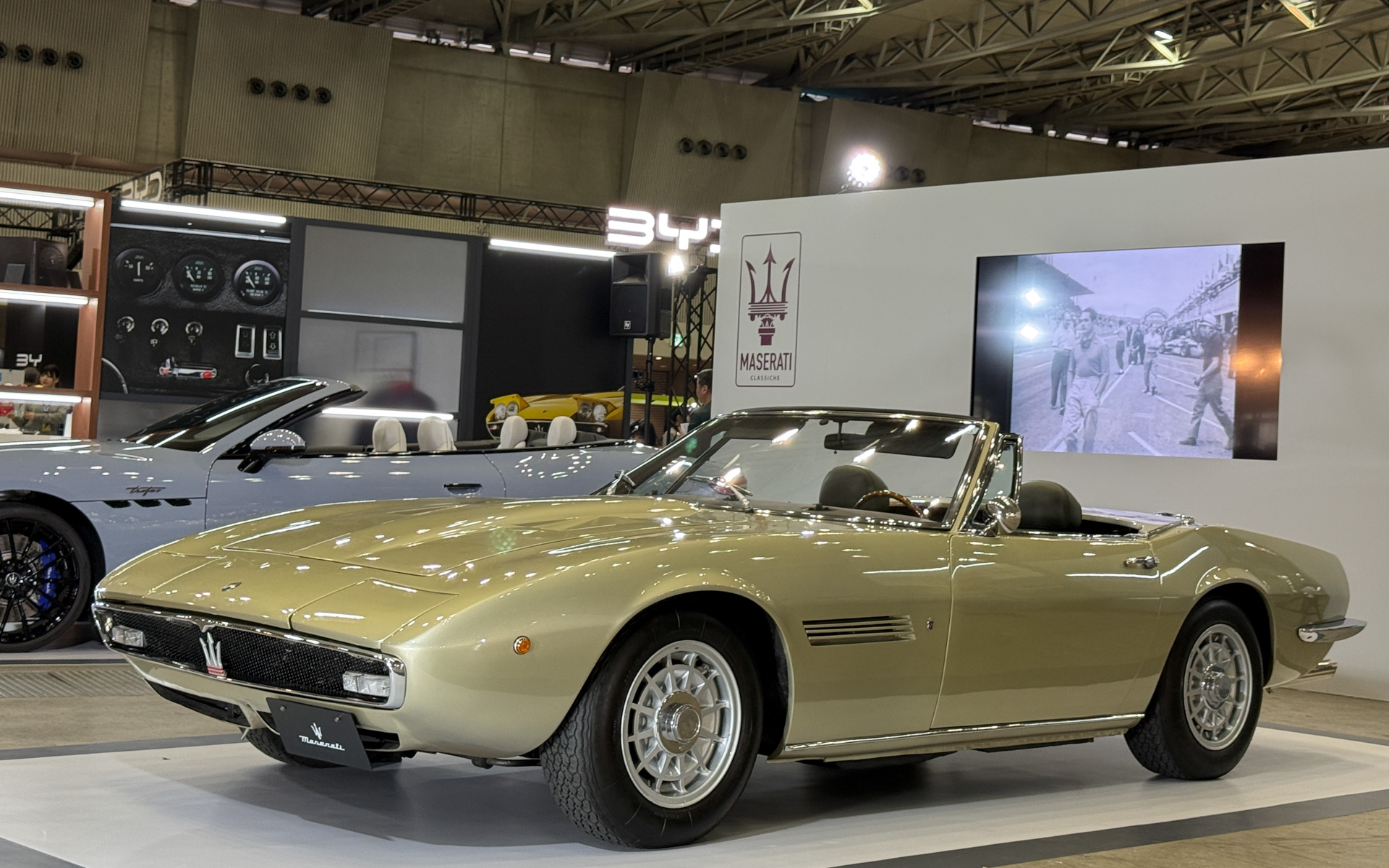 展示車両の初代「ギブリ スパイダー」。砂漠の風が車名の由来という2ドア2シータークーペモデルである「ギブリ」(1966年~1973年)のオープントップモデル。1969~1973年に、世界でわずか125台のみの生産だったため、マセラティ・ロードカーにおいて希少性の最も高いモデル。ギブリから採用をはじめたリトラクタブルヘッドライトを搭載。洗練されたクラシックなプロポーションとエレガントなラインを持つ、グランツーリングカー。4.7リッターエンジンを搭載。最高速265km/h。デザインはカロッツェリア・ギア在籍時のジョルジェット・ジウジアーロ氏によるもので、彼の最高傑作の1つとして高い評価を得ている