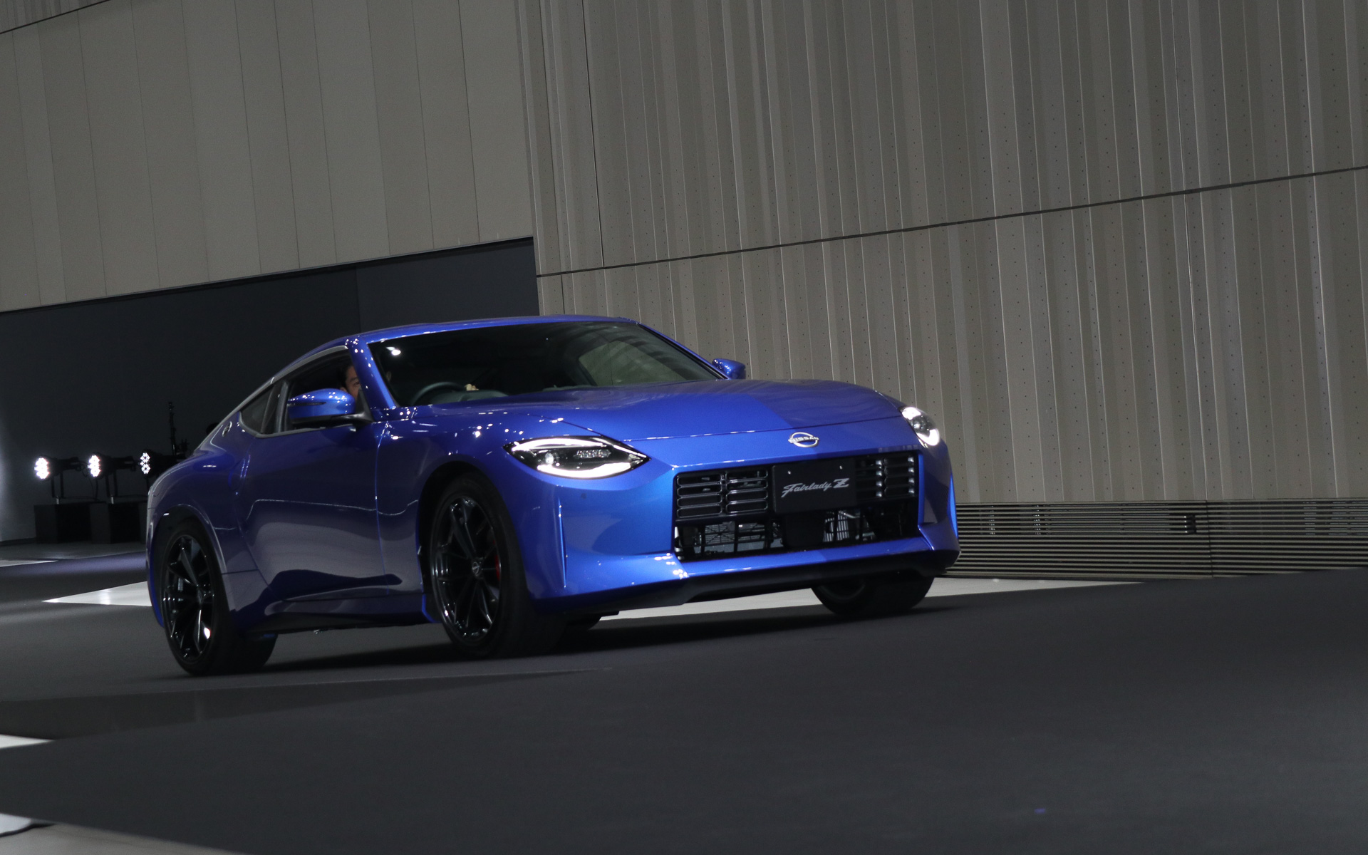 日産ホール側のシャッターが開いて「ワンガンブルー」の「フェアレディZ」が登場。ステアリングを握る鈴木さんはそのままゆっくりとフェアレディZを走らせ、日産グローバル本社ギャラリーのステージ上に上がった