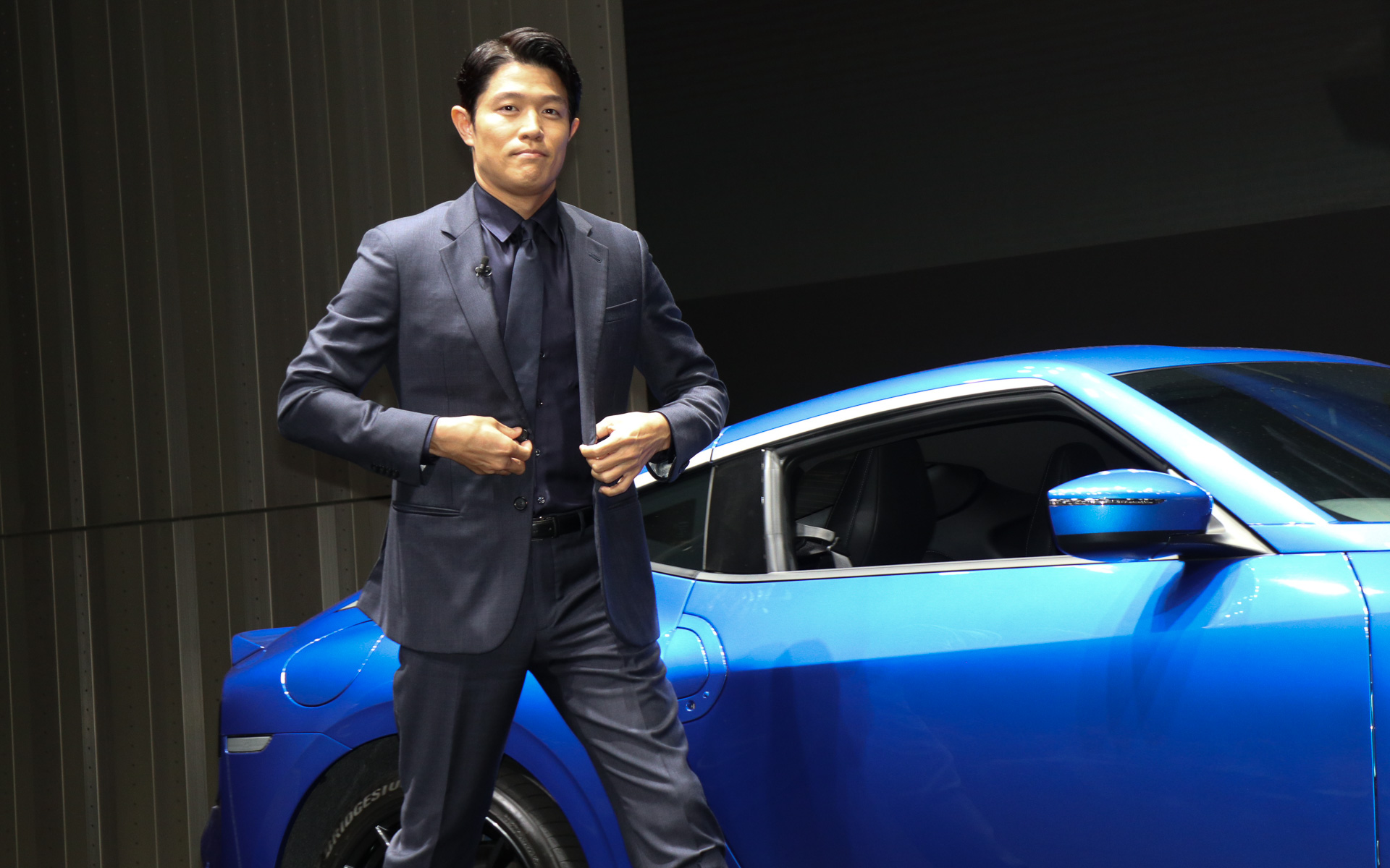 日産ホール側のシャッターが開いて「ワンガンブルー」の「フェアレディZ」が登場。ステアリングを握る鈴木さんはそのままゆっくりとフェアレディZを走らせ、日産グローバル本社ギャラリーのステージ上に上がった