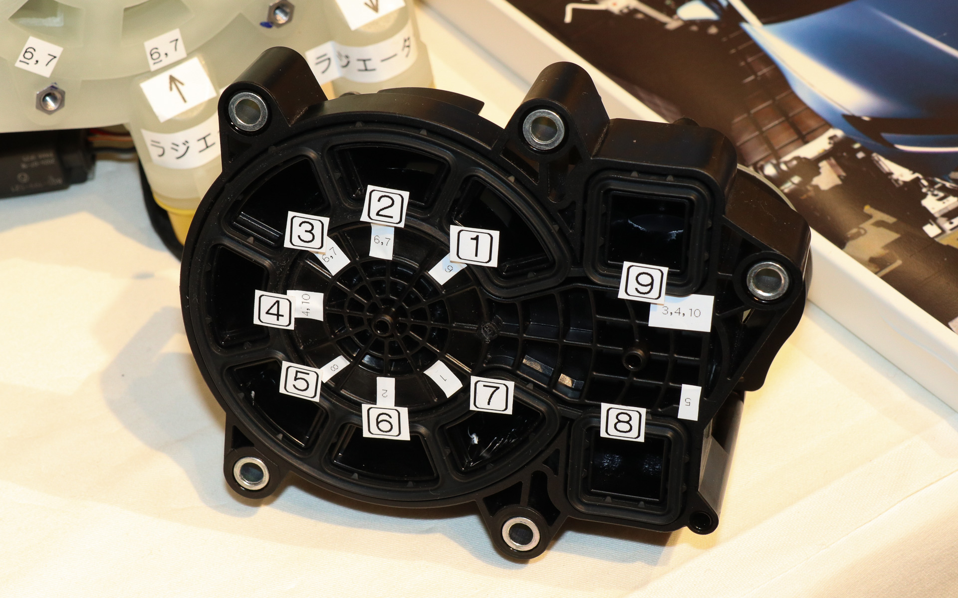 解析用に入手したSU7 Maxのリザーバータンクとバルブ切り替えユニット。本来は組み合わされているが、LLCが流れる経路がどのように対応しているか調べるために取り外し、番号を振ったシールを貼り付けて解析を行なった