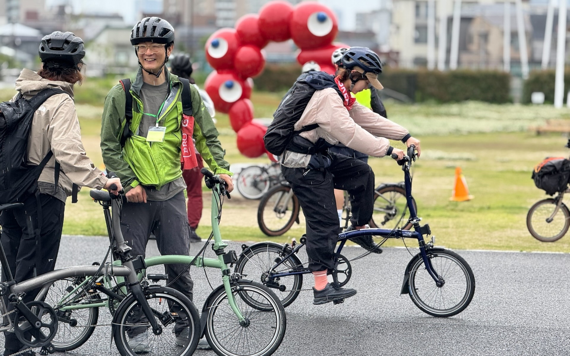 ミャクミャクのモニュメントが置かれていた此花区の正蓮寺川公園付近を通過するブロンプトンの車列。雨が降り始めたが、参加者は楽しそう