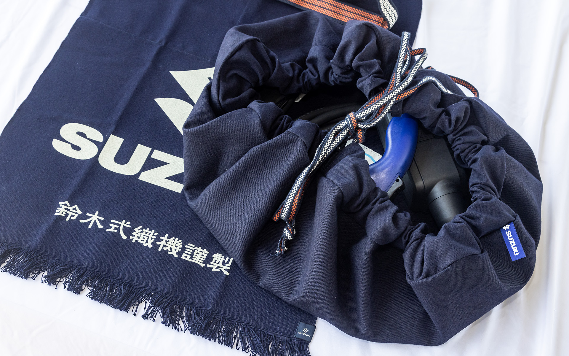 約100年前に作られた鈴木式織機で織られた生地を使ったEV充電ケーブル収納袋。下に見える鈴木式織機 前掛けは同社のECサイト「<a href="https://s-mall.jp/" class="n" target="_blank">S-MALL</a>」で購入可能