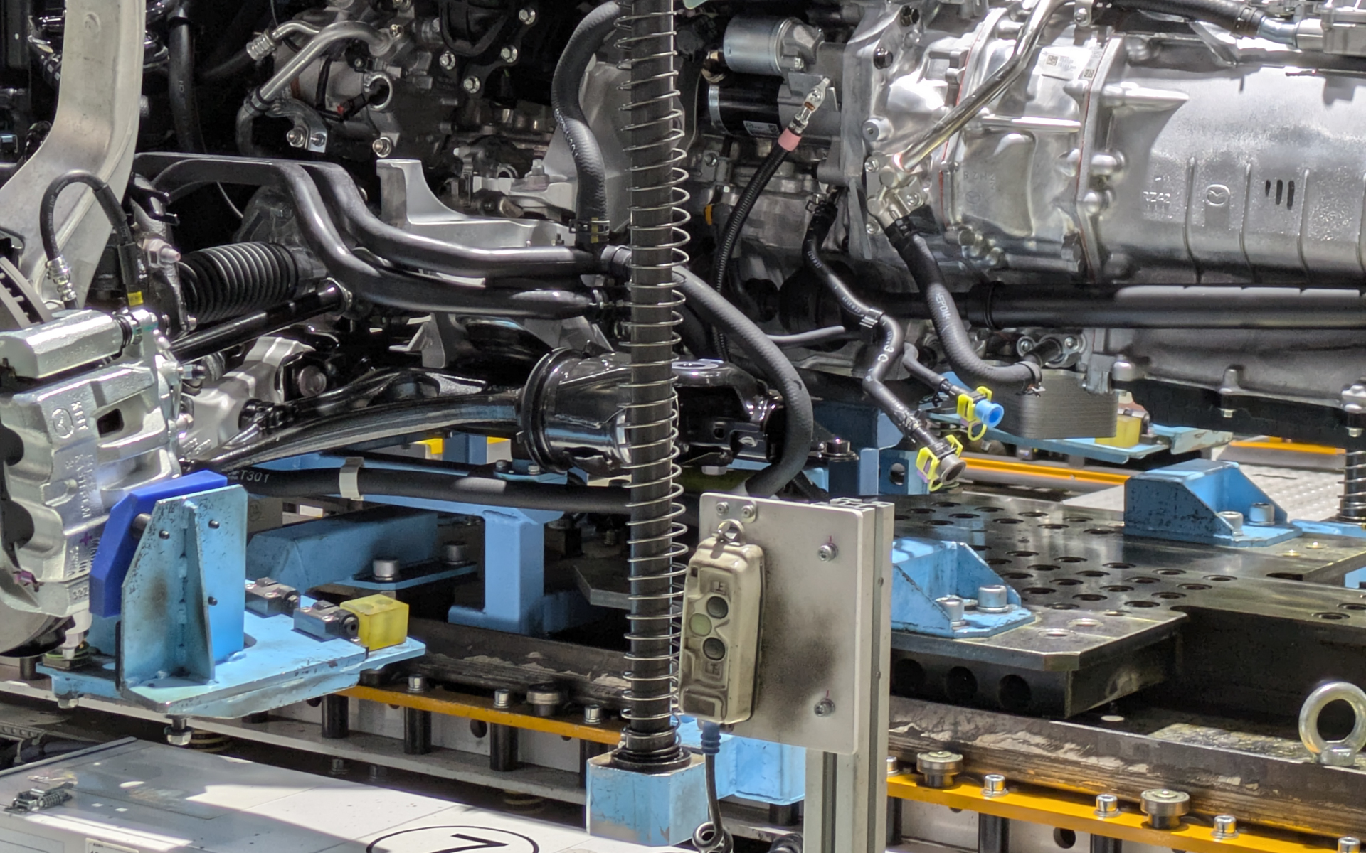 車種によって異なる取り付け部分については、位置決め具（水色や黄色の部品）の取り付け、取り外しのみで簡単に切り替え可能な設備にしてあり、同一工程での組み立てを可能としている