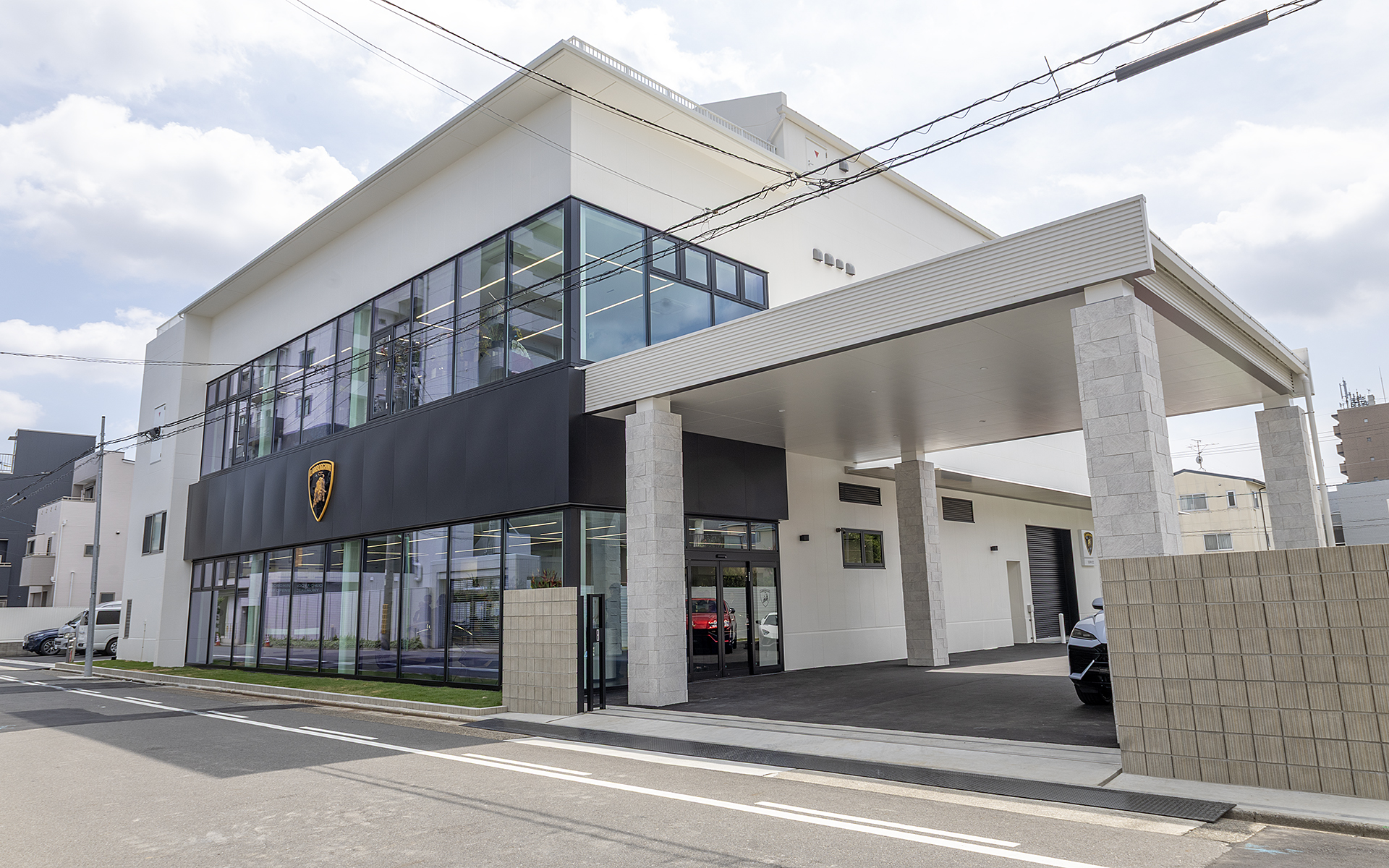 ランボルギーニ名古屋中央は愛知県名古屋市昭和区白金3-1-9に新設。正式オープンは2025年8月1日。ガラス張りの1階と2階がショールームで、奥の1～3階がサービス工場などとなる