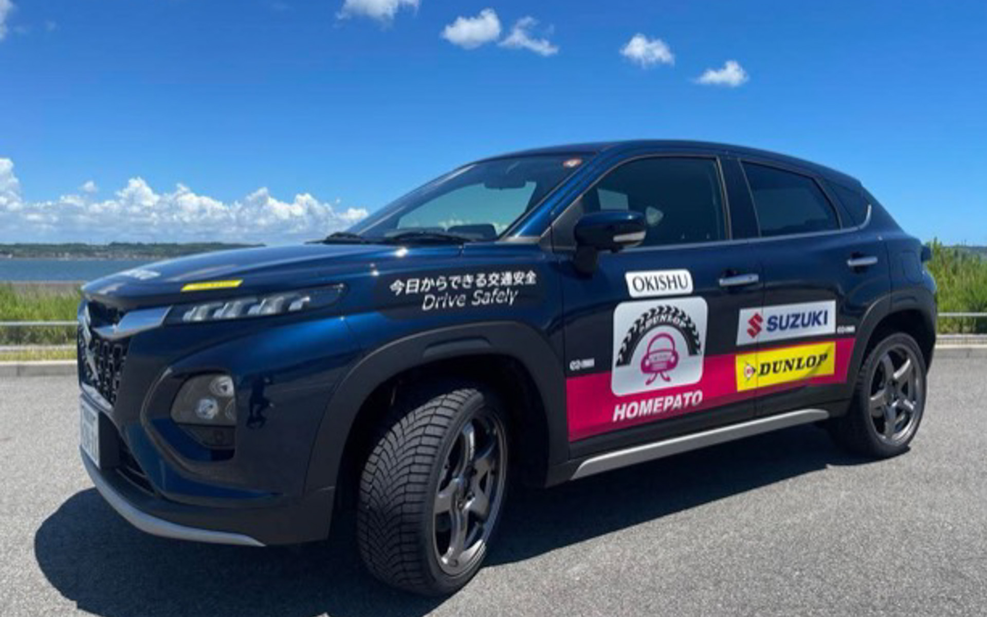 新しくなったOKISHU号は、スズキ・フロンクス！　ダークなボディカラーにホワイトのSUZUKIとENKEI、ピンクのシュー子、イエローのDUNLOPが映えますよね。わるい運転を叱るのではなく、よい運転を褒める「ホメドライブ」の精神を受け継ぎ、HOMEPATOのロゴも入っています