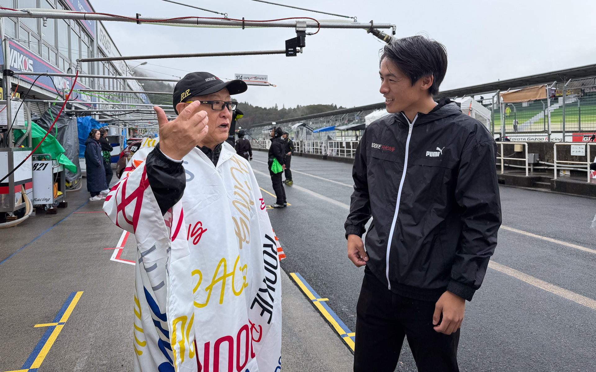 レインコート姿でスタッフと打ち合わせるトヨタ自動車株式会社 代表取締役会長 豊田章男氏（左）