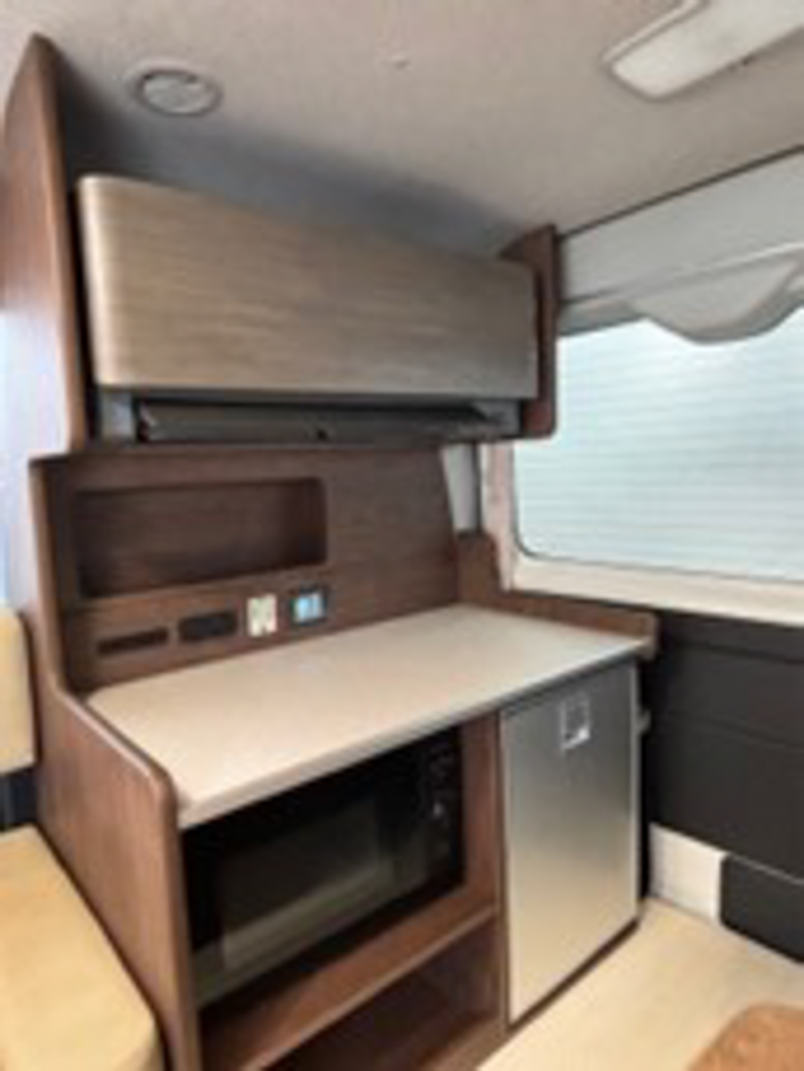 後部には家庭用エアコンと電子レンジを標準装備。ベットスペースは、対角線上に寝る独特な配置し、書斎としても使えるデスクも完備する