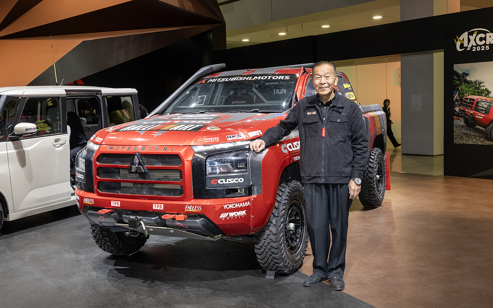 アジアクロスカントリーラリー2025の優勝車両となるトライトン。ブースにいた増岡監督に、車両の隣に立ってもらった