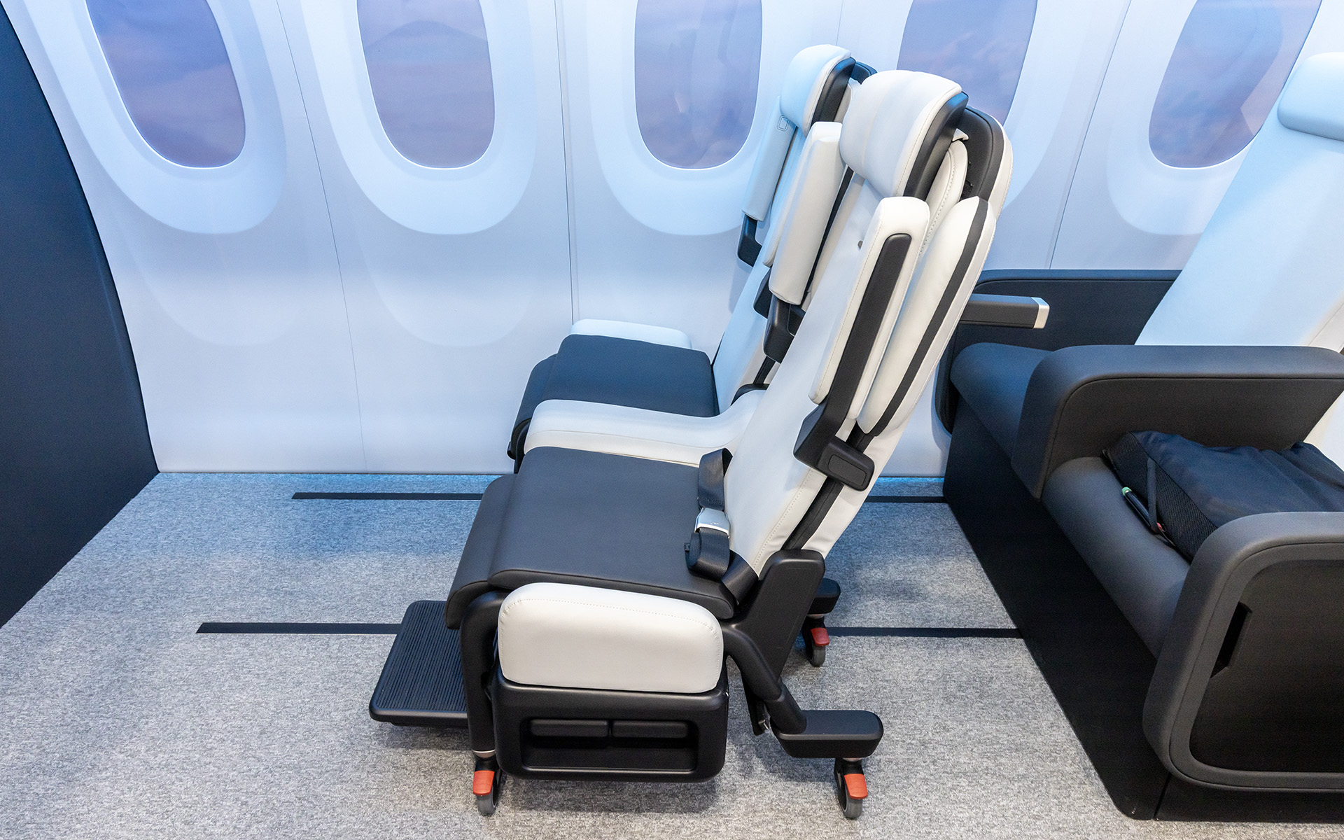 JAXAと研究開発する航空機向けのシート「ウェルボヤージュ・シート」。フロアへの固定方法は従来と同様。ただ、シートバックに介助者用のハンドルが付くためテーブルや後方席用のモニター設置は不可能。機内での位置は最前列や最後列などある程度限定されることになりそう