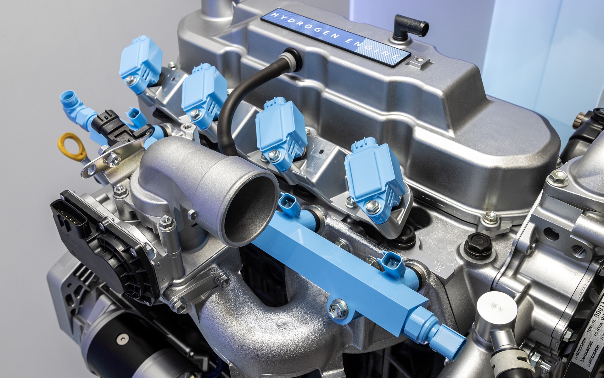参考出品となる水素エンジン。主な変更点は水色で塗られた部分で示され、後付のターボチャージャーや、デリバリーパイプと点火コイル＆スパークプラグ程度とのこと