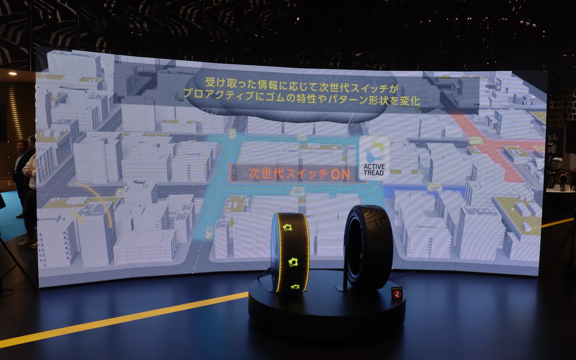 左側に置かれたタイヤ型のディスプレイで、タイヤの特性や形状を事前に最適化させるイメージを表現している