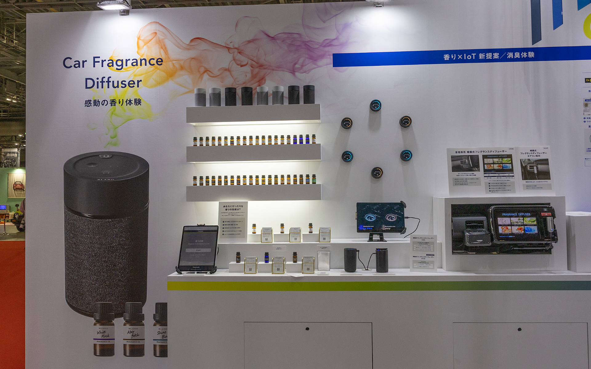 参考出展の車種専用噴霧式フレグランスディフューザーの展示。右端にはこちらも参考出展の噴霧式フレグランスディフューザー エアコン取り付けタイプ（銀色のもの）が展示されている