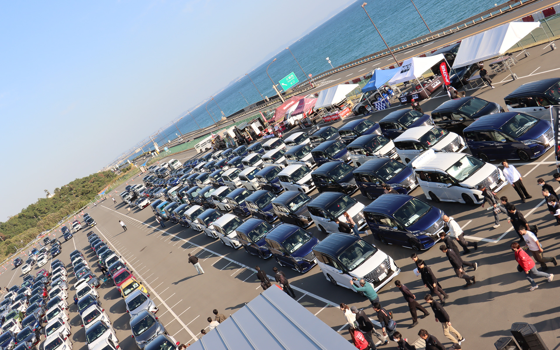 会場となった大磯ロングビーチ 第1駐車場では、中央のロッカーハウスを挟んで出入り口に近い東側に参加台数の多い「ノート＆ノート オーラ」「セレナ」「ミニバン」などが集まって駐車