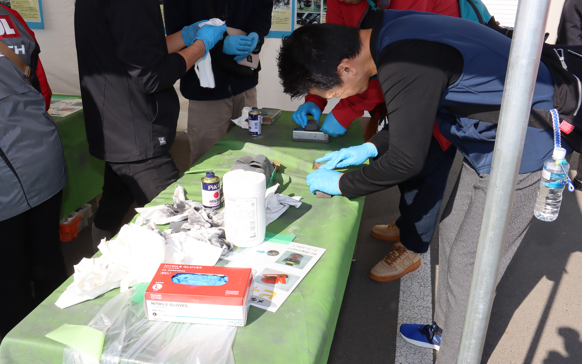 モノづくり体験ブースではイベント参加の記念品にもなるメダル作成を実施。事前に打ち抜かれて片面に刻印したメダルの無地面に油圧プレスでロゴを刻印したあと、紙やすりと研磨剤を使ってピカピカに磨き上げていく