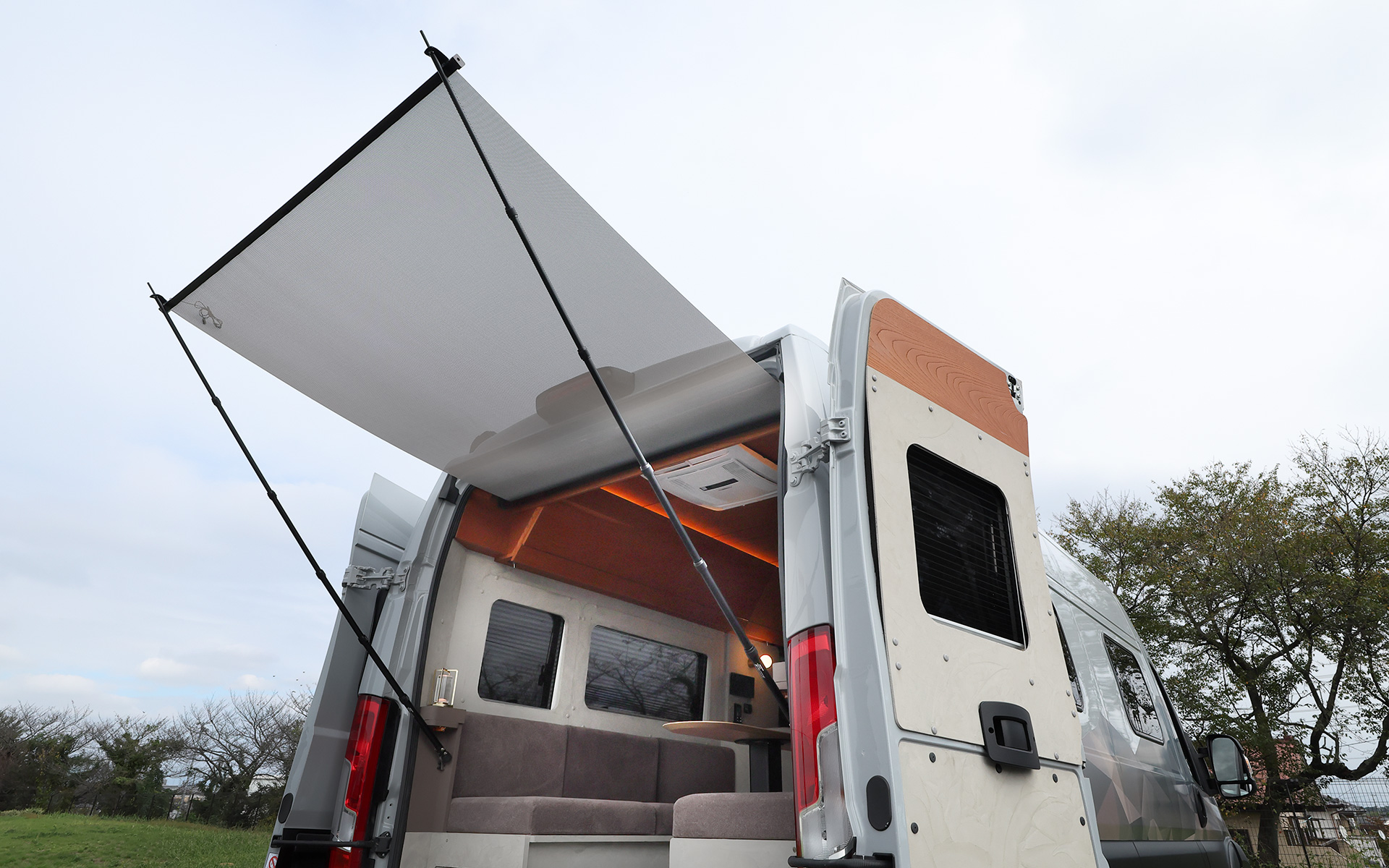 インテリアではブリッドと共同開発したキャンピングカー専用のバケットシートを運転席＆助手席にセット。また“移動する別荘”を目指し、天然素材のケヤキの木目を生かしたデザインで上質感を演出する吊り戸棚、対面式のベンチソファー、ベンチソファーと組み合わせることで簡単にセットアップできるベッド（1800×1800mm）、大型のリアオープンデッキ、電子レンジと85Lの冷蔵庫を1か所にレイアウトしたキッチン、外部電源による充電と走行充電で電力を確保できるサブバッテリ（リン酸鉄リチウムイオン/5kWh）などを装備。タープやサンシェードなども付属する