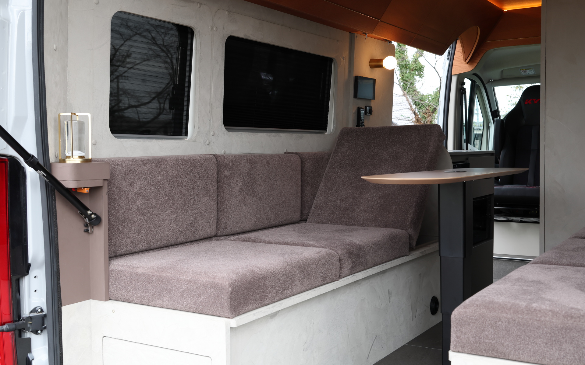 インテリアではブリッドと共同開発したキャンピングカー専用のバケットシートを運転席＆助手席にセット。また“移動する別荘”を目指し、天然素材のケヤキの木目を生かしたデザインで上質感を演出する吊り戸棚、対面式のベンチソファー、ベンチソファーと組み合わせることで簡単にセットアップできるベッド（1800×1800mm）、大型のリアオープンデッキ、電子レンジと85Lの冷蔵庫を1か所にレイアウトしたキッチン、外部電源による充電と走行充電で電力を確保できるサブバッテリ（リン酸鉄リチウムイオン/5kWh）などを装備。タープやサンシェードなども付属する