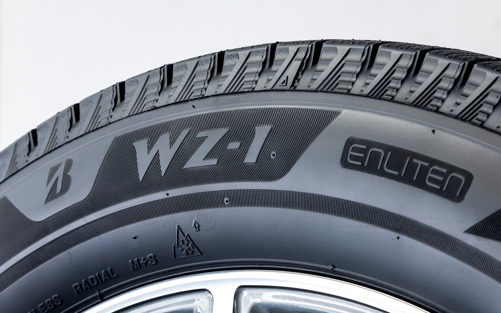 WZ-1は商品設計基盤技術「ENLITEN」（エンライトン）を乗用車用スタッドレスタイヤとして初搭載し、ブリザック史上で“断トツ”のアイスコントロール性を実現するとともに、サステナビリティへも貢献する製品へと進化。トレッドパターンではブロックまわりへの水の回り込みを抑制するL字ブロック、ブロック面への水の浸入を抑えるL字タンクサイプを採用するとともに、独自技術「発泡ゴム」に業界初の新技術「親水性向上ポリマー」を配合した「Wコンタクト発泡ゴム」を搭載。ゴムの気泡による水の除去に加え、親水性向上ポリマーとわずかに残った水の分子間力により、滑る原因となっていた水をもグリップ力へと変換することに成功