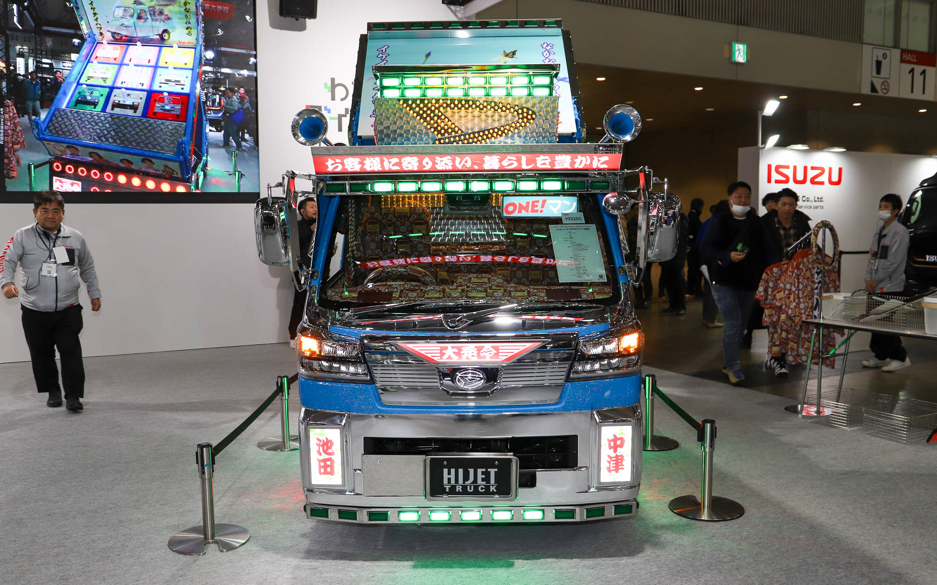 ダイハツのスローガン「お客様に寄り添い、暮らしを豊かに」を高々と掲げ、本社のある大阪府池田市と工場のある大分県中津市の地名を用いた行灯が前方を照らす