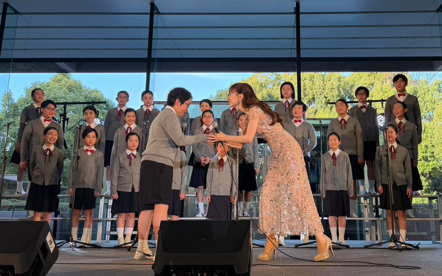 合唱の感想を述べた本郷小学校合唱団の代表に握手を求めるMay J.さん