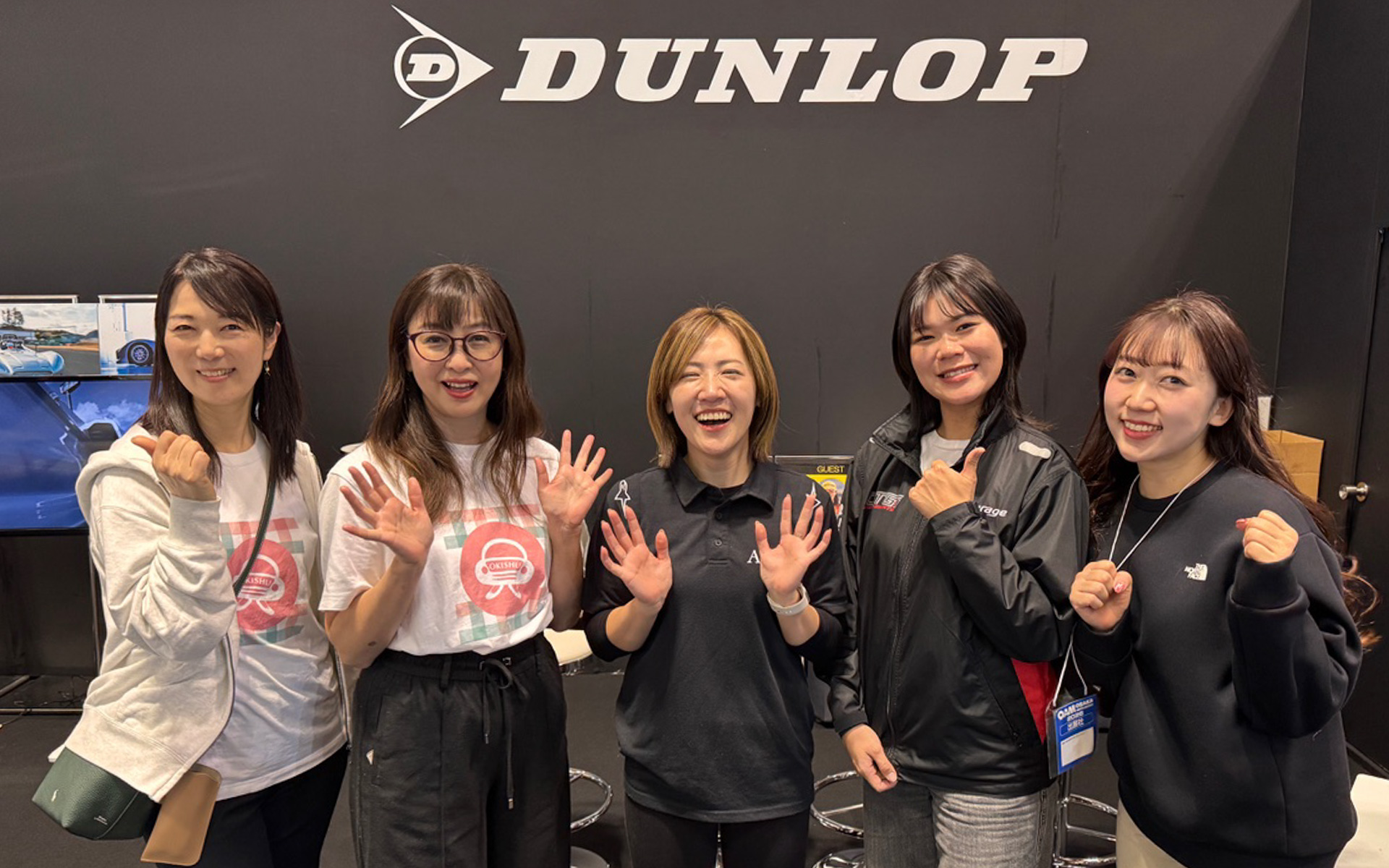 大阪オートメッセ2026「OKISHU×DUNLOP」ブースに集結した業界女子たち。右から、英語ペラペラでYouTubeの撮影・編集・喋りまで頑張ってくれた華音ちゃん。レーシングドライバーの翁長実希ちゃん、ドライバーだけでなく監督・ドライバー育成にも挑戦中の三浦愛ちゃん、カーライフエッセイスト吉田由美さん、私・まるも亜希子です