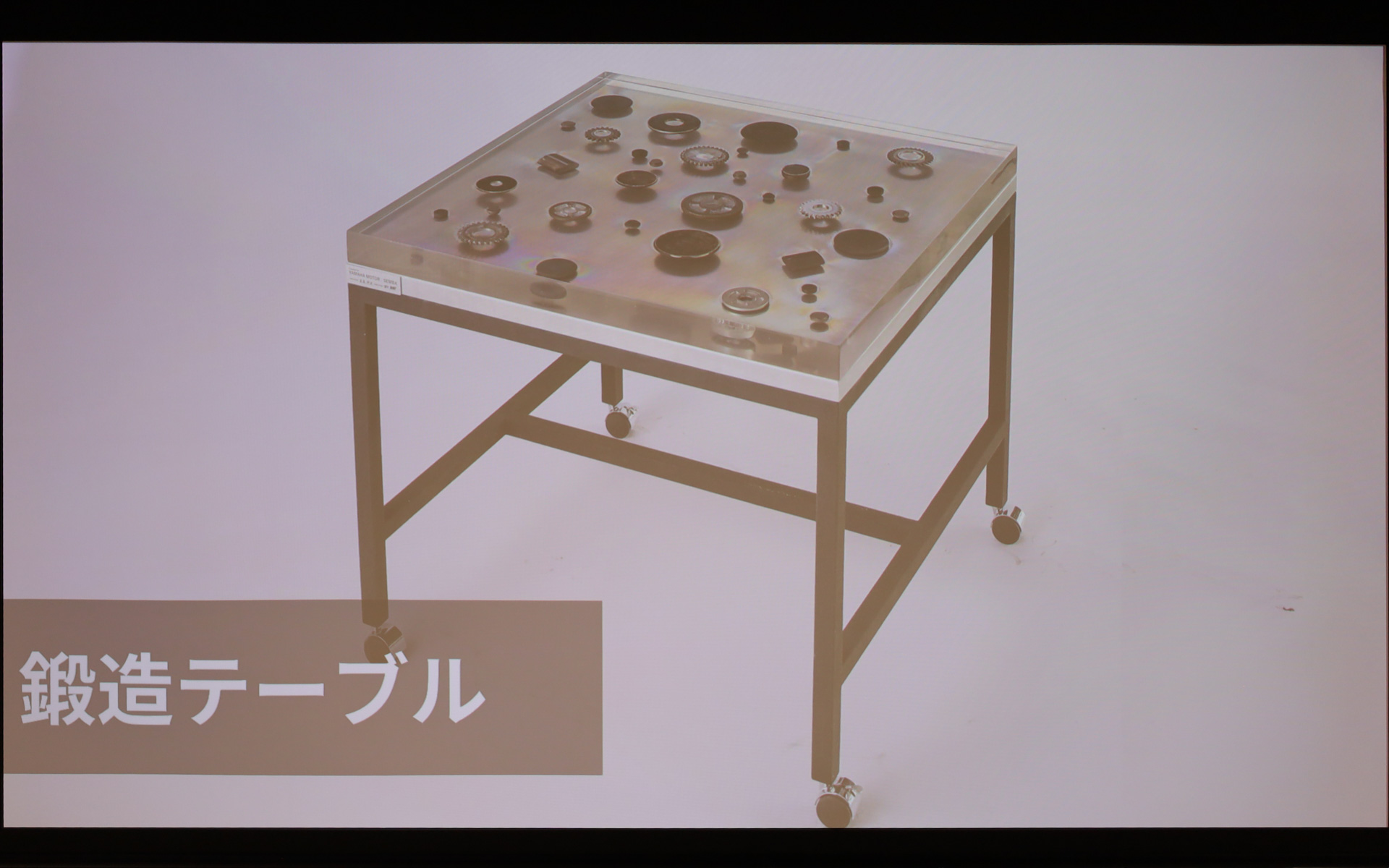 ヤマハ発動機のモノづくりを支える「鍛造（たんぞう）」技術をデザインの核とし、金属の力強さと美しさを可視化。鍛造で制作されるバイク部品を透明度の高いレジンに封入し、5層構造で流し込むことで立体的に表現した。50mmの厚みの中で部材を配置する位置や高さを変えることで、見る角度によって表情が変わる。表面をあえてレジンを染み込ませずに、金属の質感を触ることができる部分も残した。普段は意識されることのない内部部品を主役として昇華することで、そこに込められたヤマハ発動機の技術と精度の高さに触れられる仕上げにした