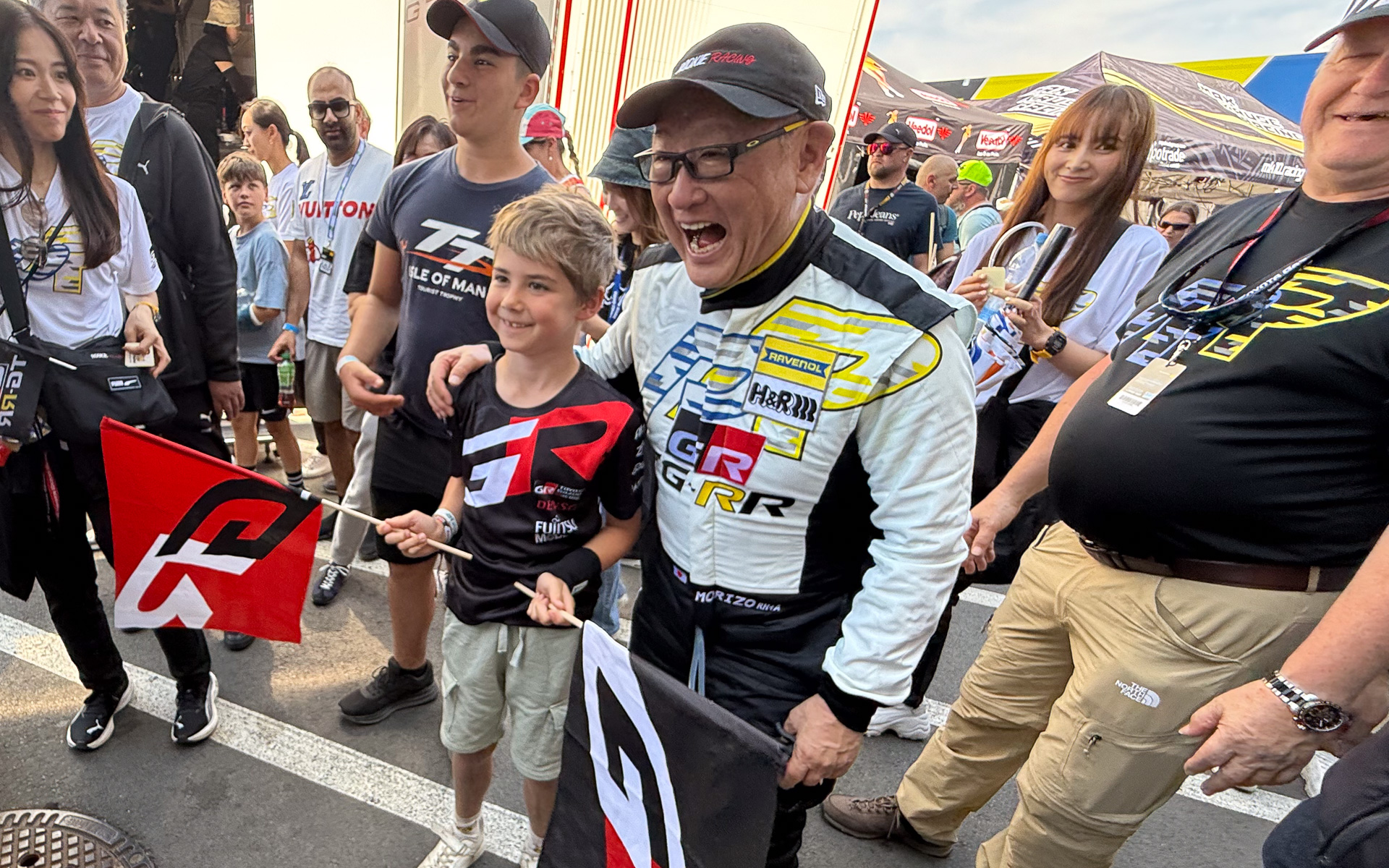 2025年のニュルブルクリンク24時間レースにて、第2スティントの9周を走り終えた後、ファンの記念撮影要望に応じていたモリゾウ選手こと、トヨタ自動車株式会社 代表取締役会長 豊田章男氏（中央右）