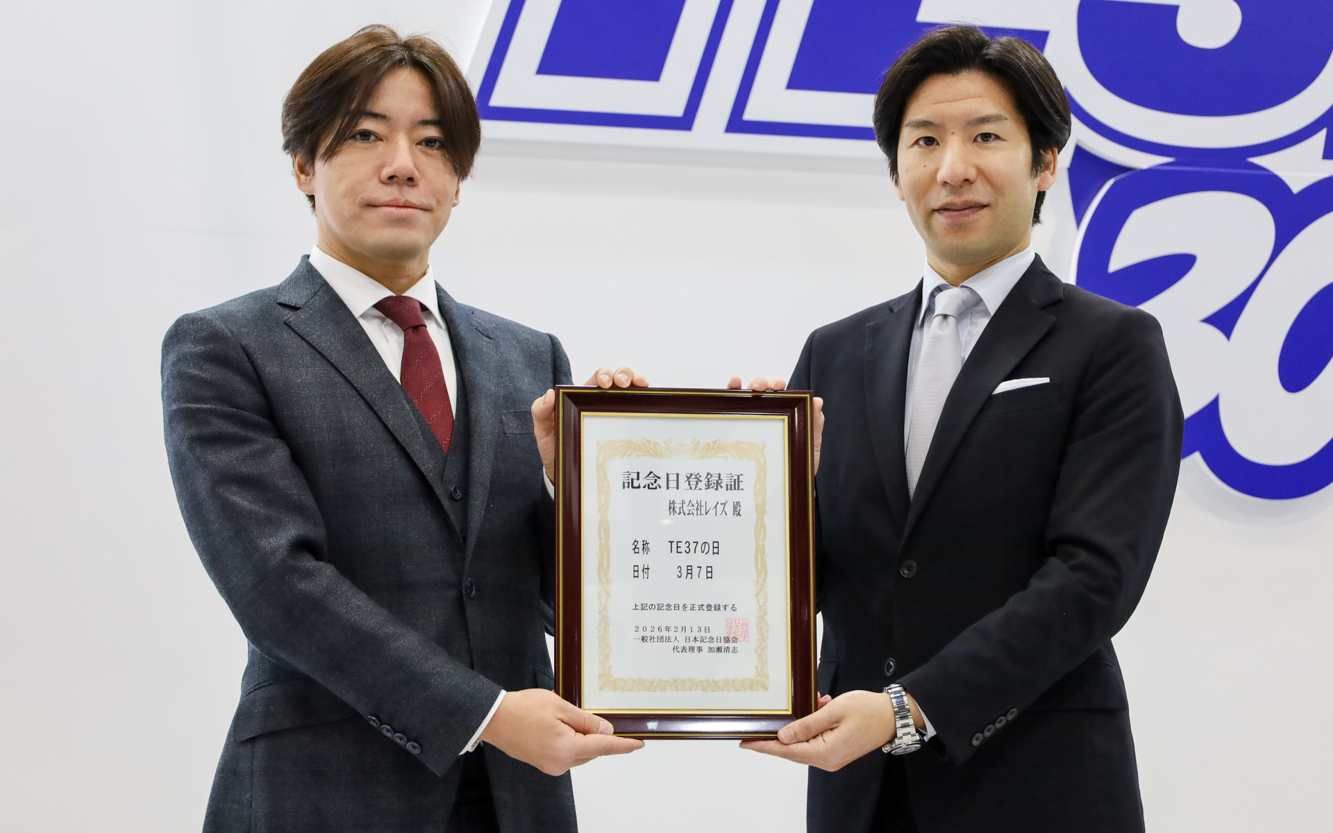 大阪オートメッセ2026の会場で実施された認定証授与式の様子。株式会社レイズ 代表取締役社長の斯波翔太郎氏（左）と日本記念日協会のスタッフ（右）