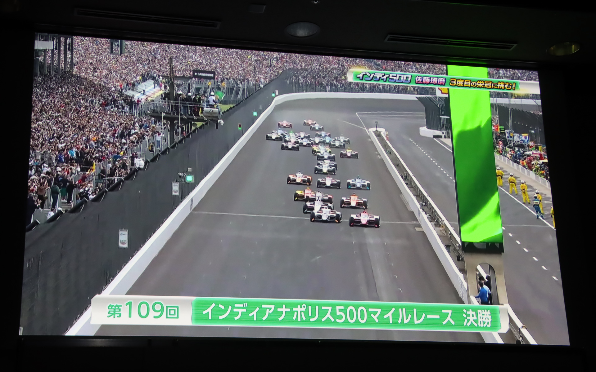 ステージ上のスクリーンで上映されたインディ500 2025年大会のダイジェスト。予選2番手からのスタートで51周をトップ走行したが、一斉にピットインしたタイミングで佐藤琢磨選手は自分のピットスペースで停止できず、大きく順位を落として9位フィッシュとなった