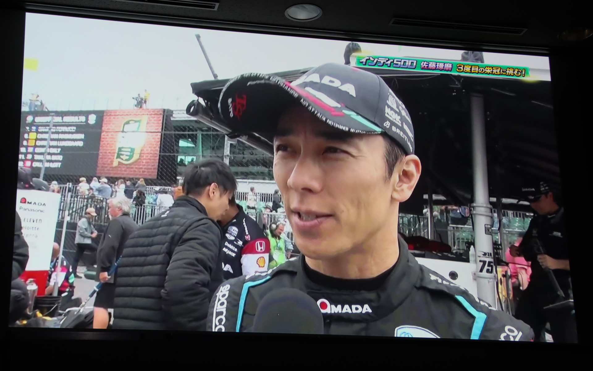 ステージ上のスクリーンで上映されたインディ500 2025年大会のダイジェスト。予選2番手からのスタートで51周をトップ走行したが、一斉にピットインしたタイミングで佐藤琢磨選手は自分のピットスペースで停止できず、大きく順位を落として9位フィッシュとなった