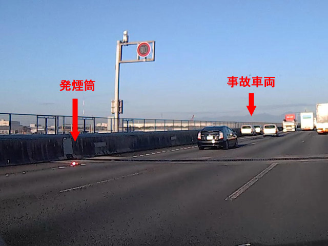 路側帯に黄色い車両、その先に発煙筒、さらにその先に事故車