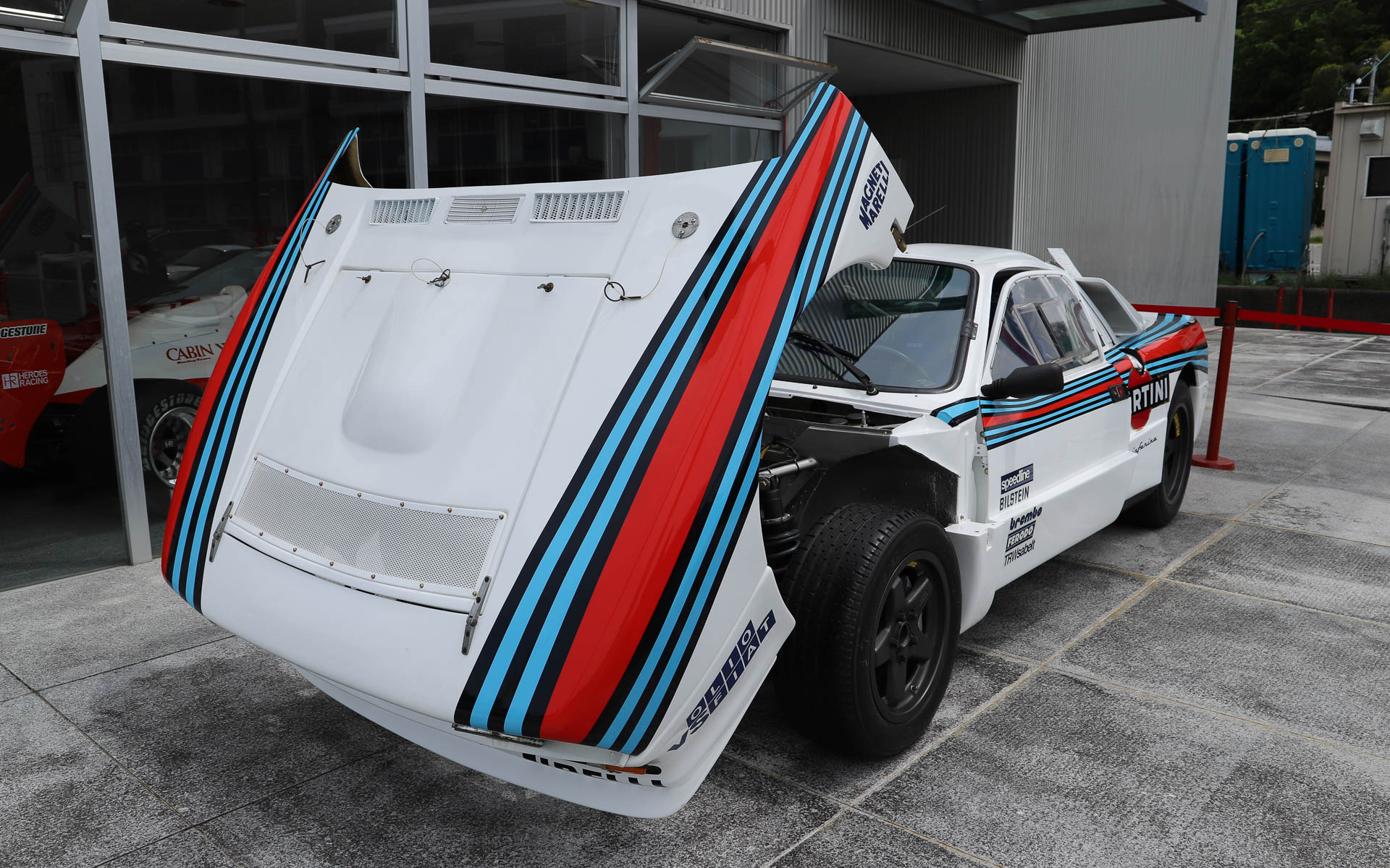 「ランチア・ラリー037」。4WDが台頭してきた1980年代のWRCに、あえてミッドシップで挑んだ車両。過酷なレースのため、現存するワークスマシンは約半数と言われている。デザインはピニンファリーナが担当した。ボディはケブラーとカーボンファイバーで構成され、当時としてはかなり軽量とされている。整備性を高めるため、エンジンルームへのアクセスがしやすいような工夫がされており、ボンネットはパイプ1本で支えるだけとなっている。エンジンは「アバルト・131」の直列4気筒エンジンをベースにチューニングし、スーパーチャージャーを搭載することで、低回転域からパワーを発揮する